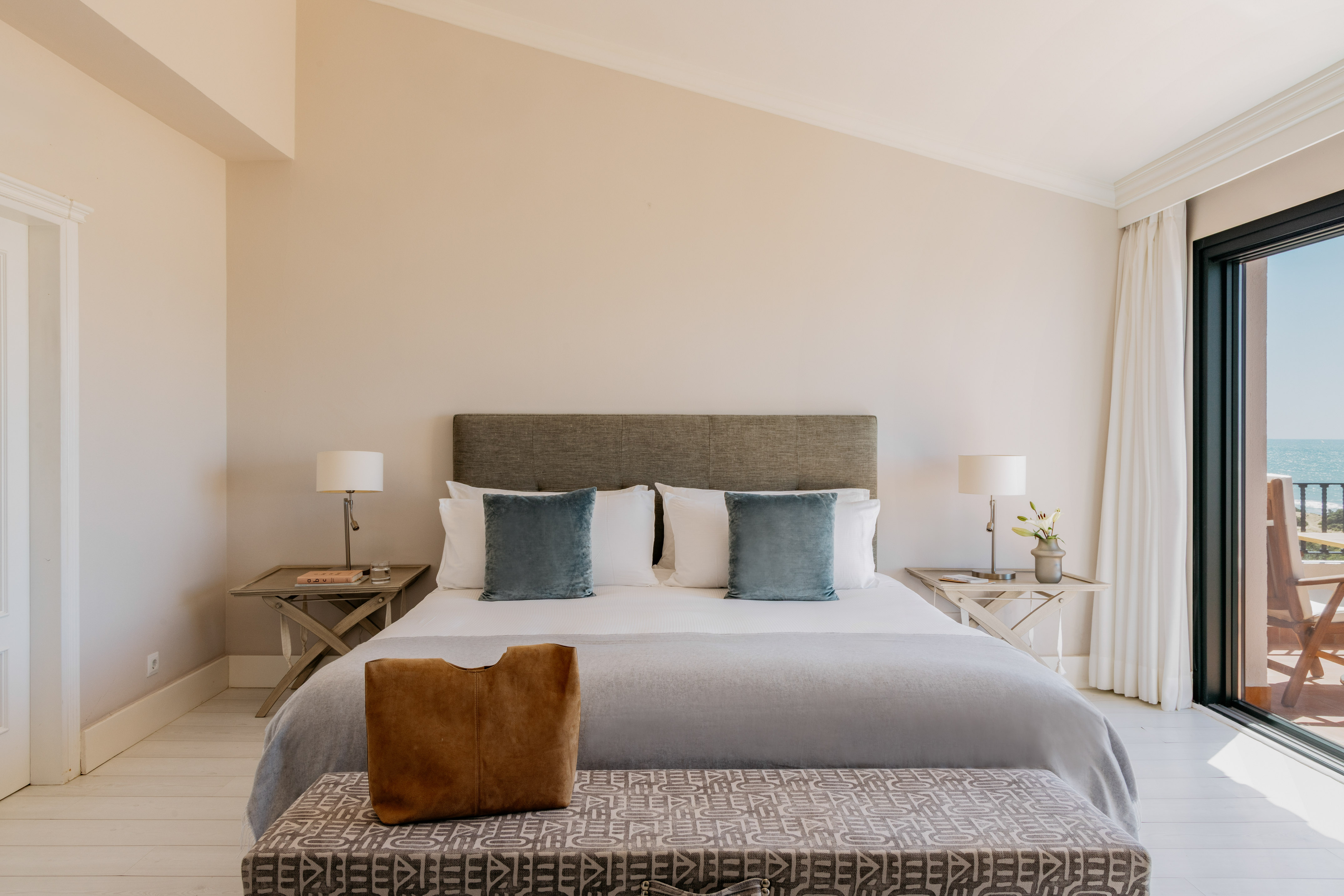 Elegant bedroom with king bed, ocean view balcony, and light decor.