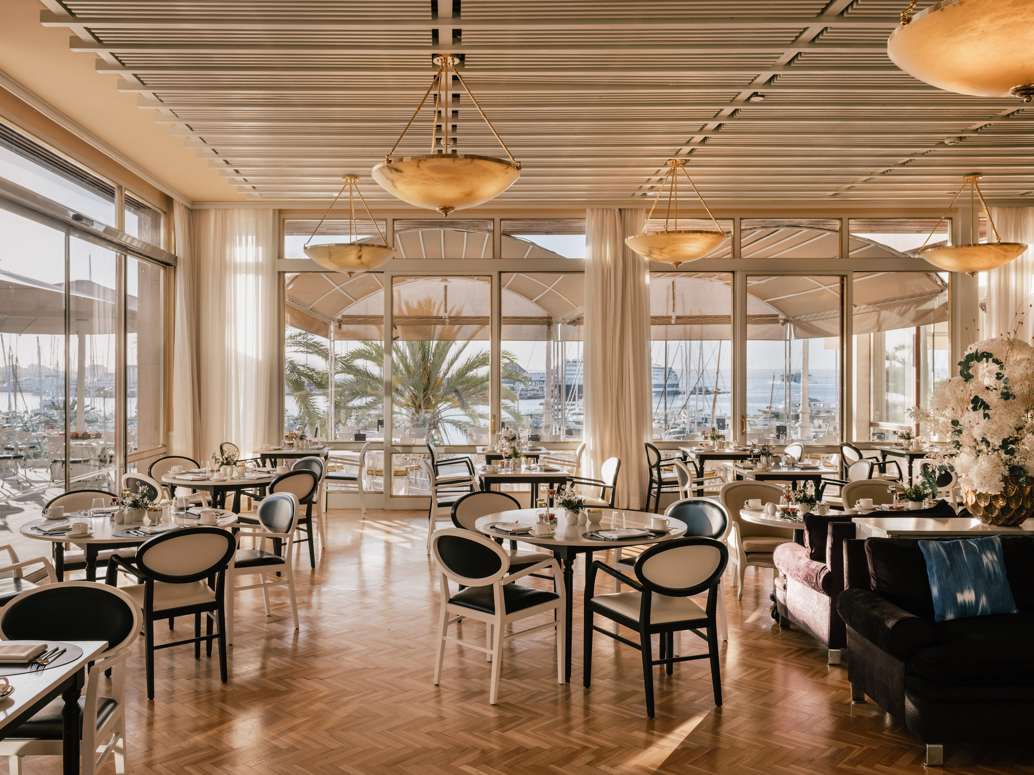 Elegant restaurant interior overlooking marina, with set dining tables and chandeliers.