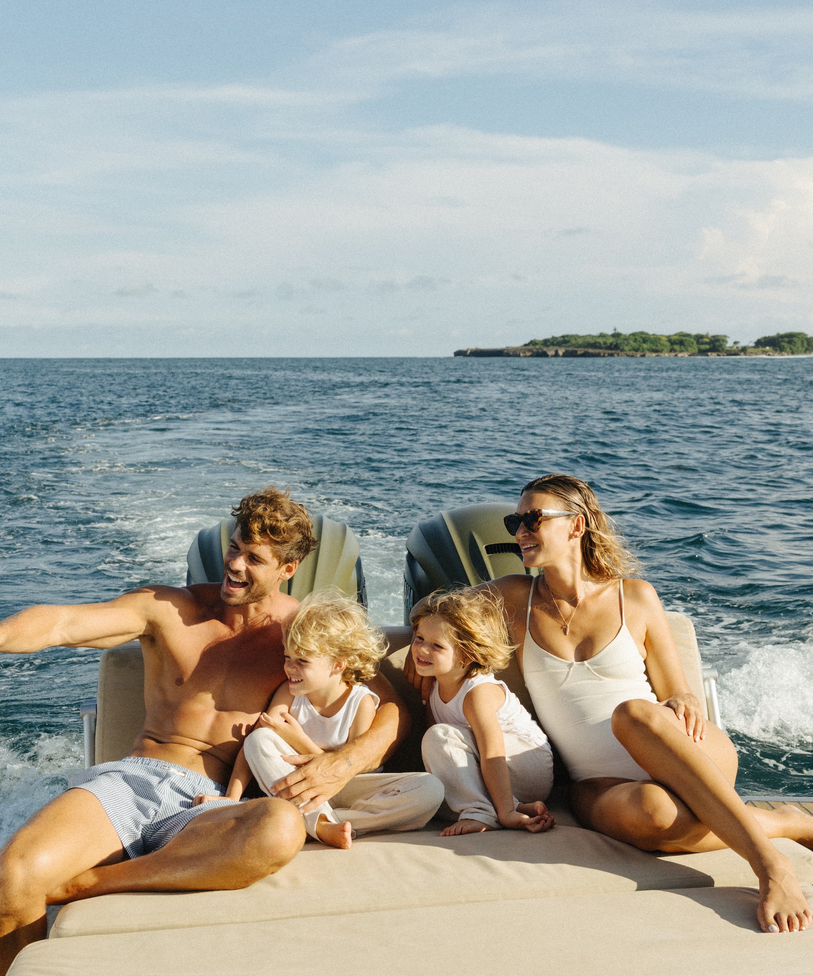 Family with two kids laughing on a boat, dad pointing to the ocean.