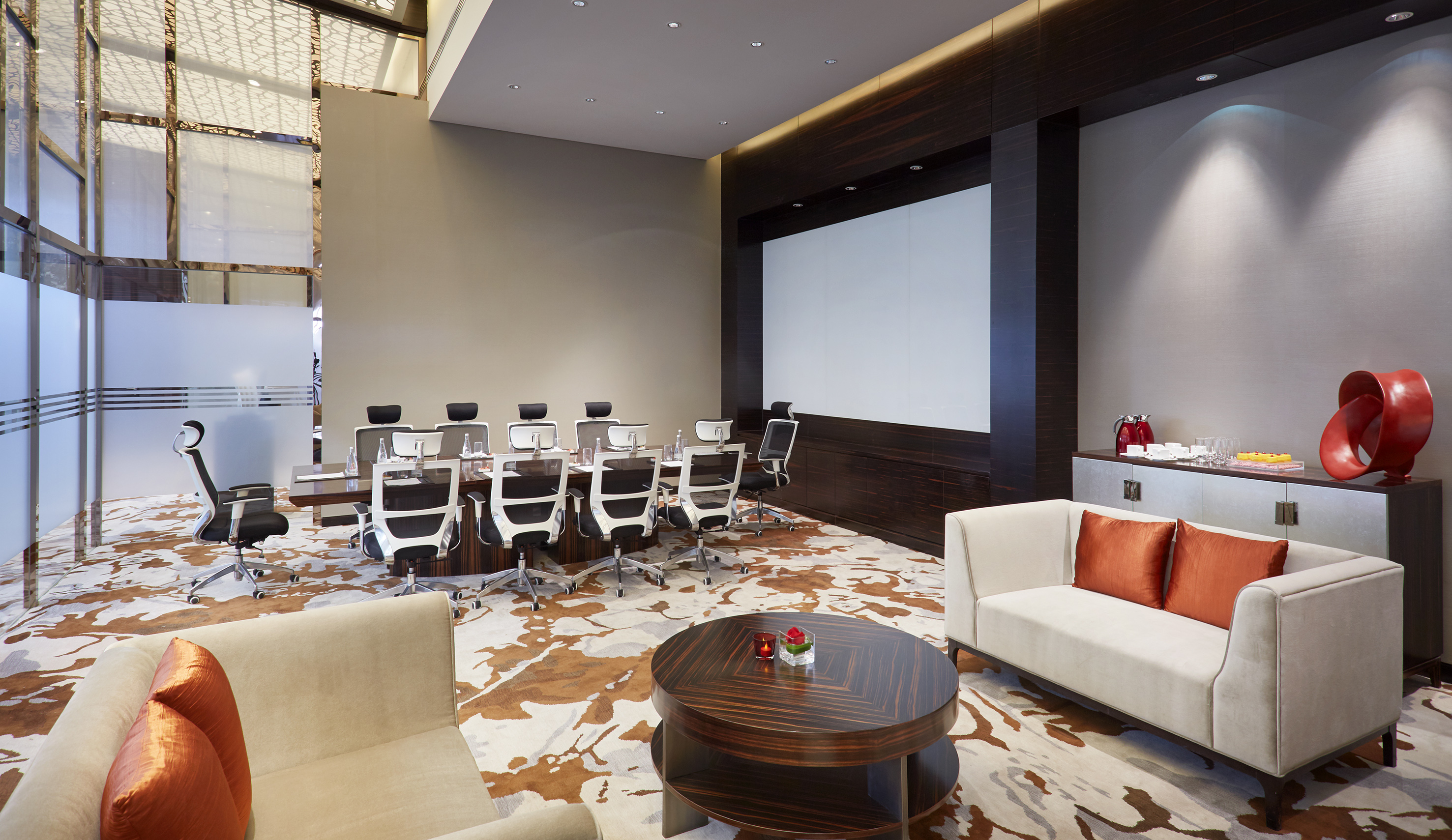 Modern meeting room with conference table, projector screen, and lounge seating.