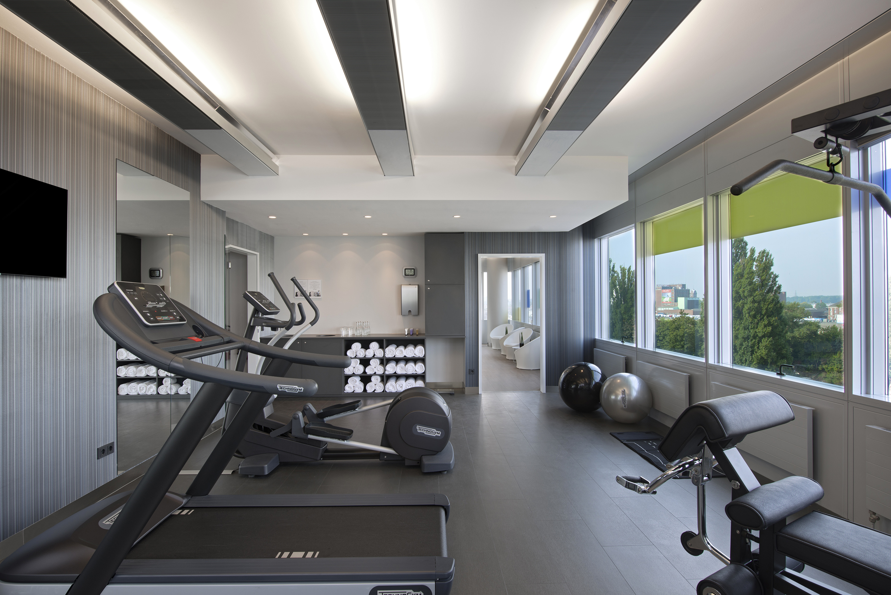Hotel fitness center with treadmills, elliptical, workout bench, and city views.