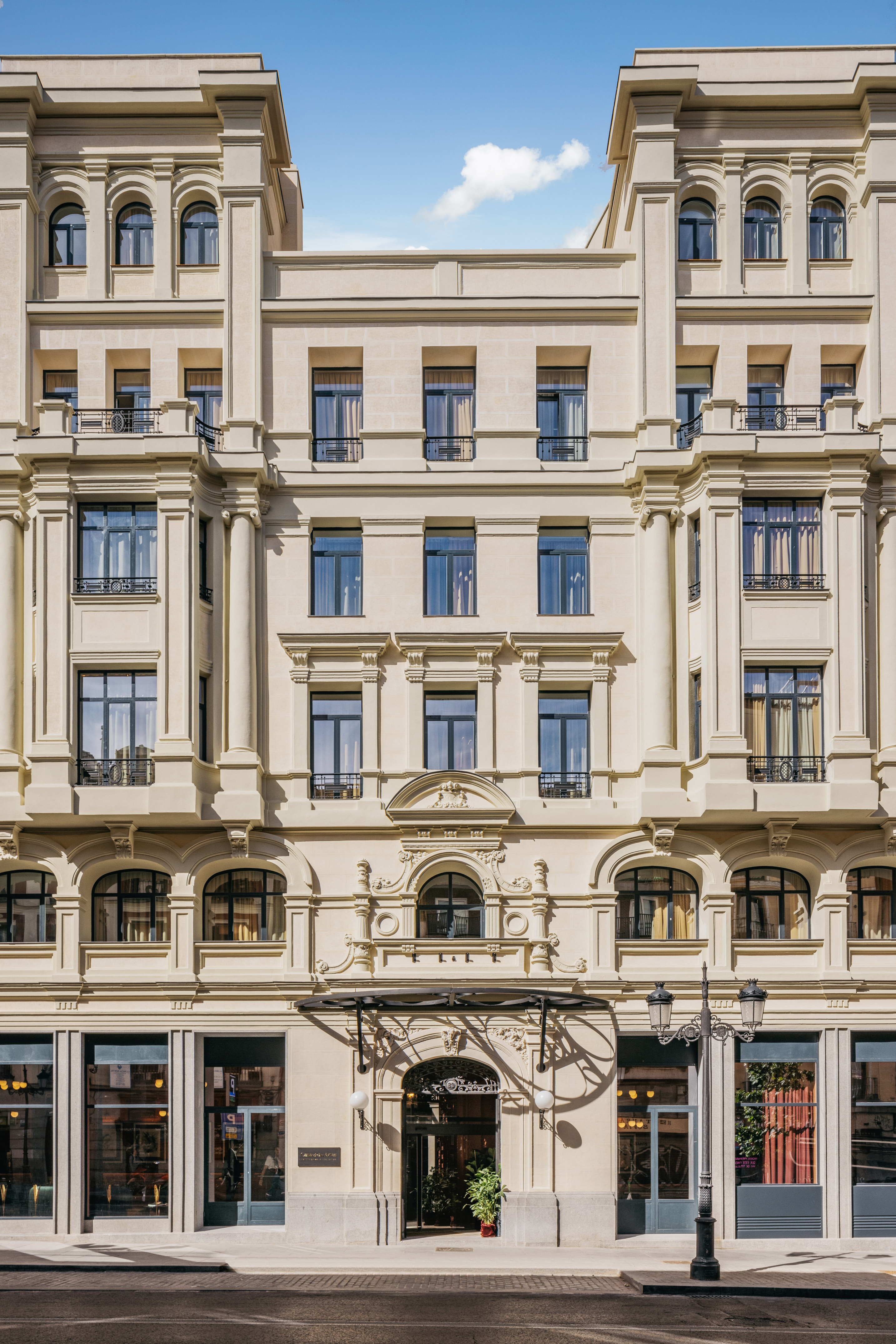Ornate cream building facade with classical columns, arched windows, street entrance.