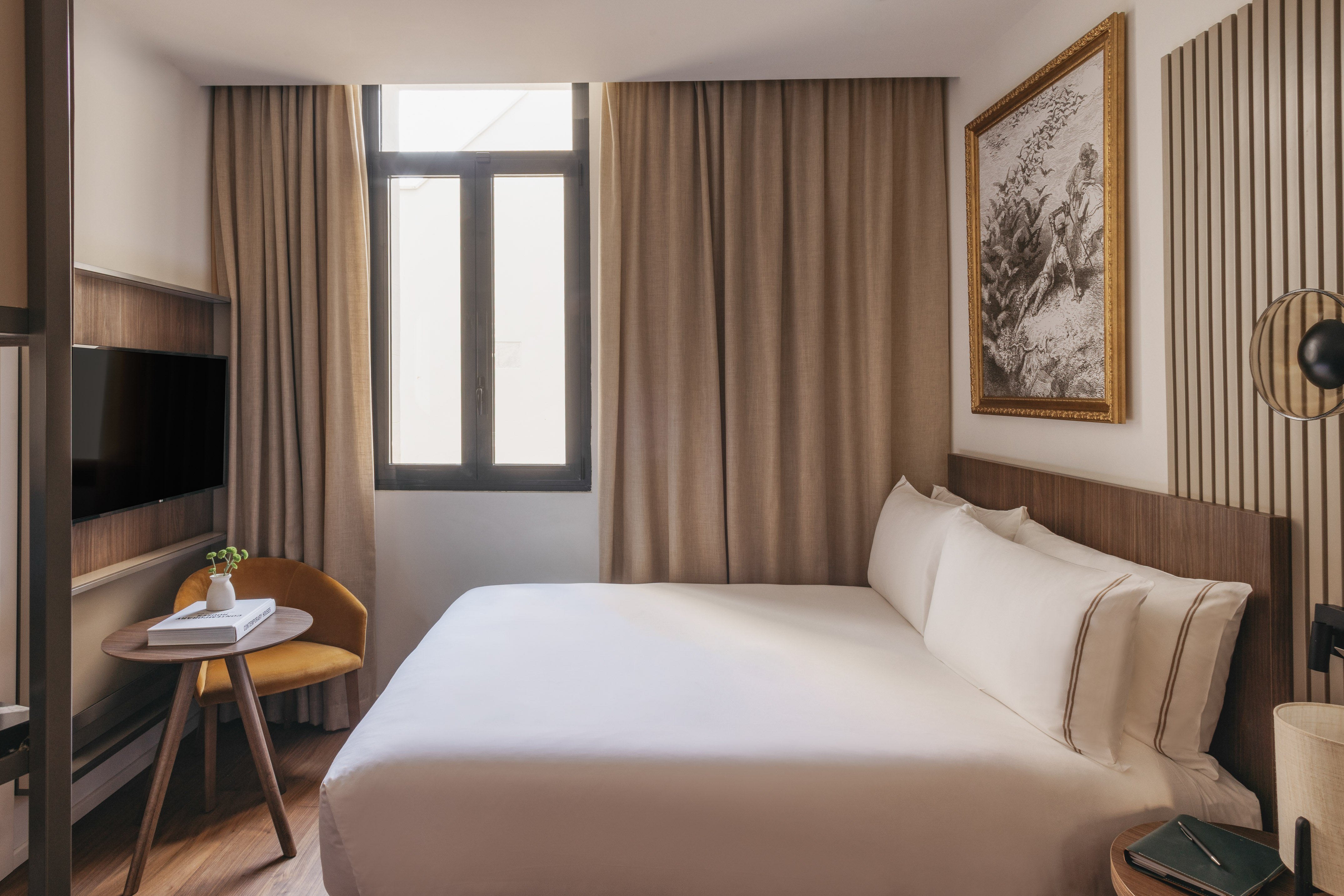 Modern hotel bedroom with large white bed, window, TV, and yellow accent chair.