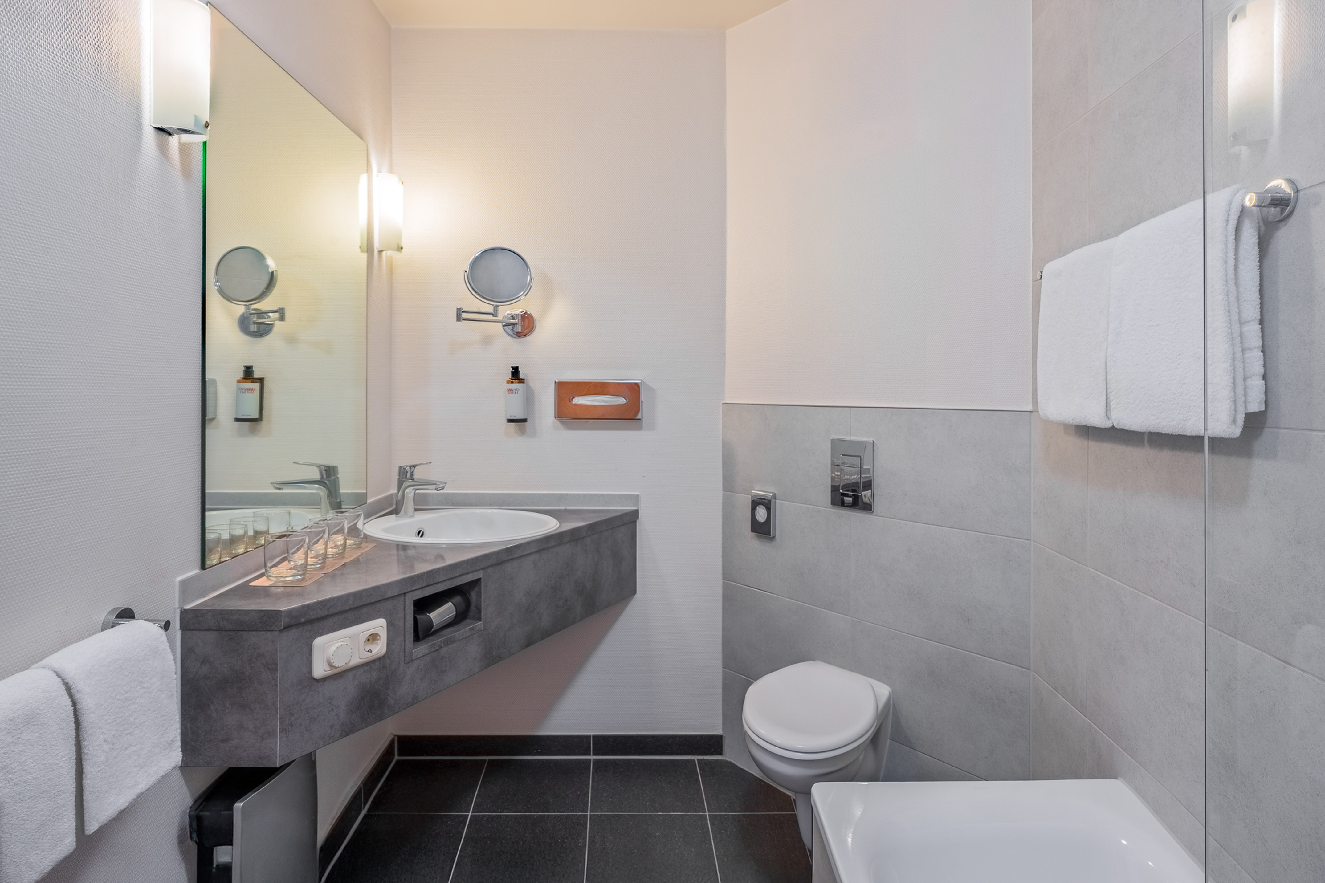 Sleek hotel bathroom with gray vanity, sink, mirror, toilet, and shower bathtub.