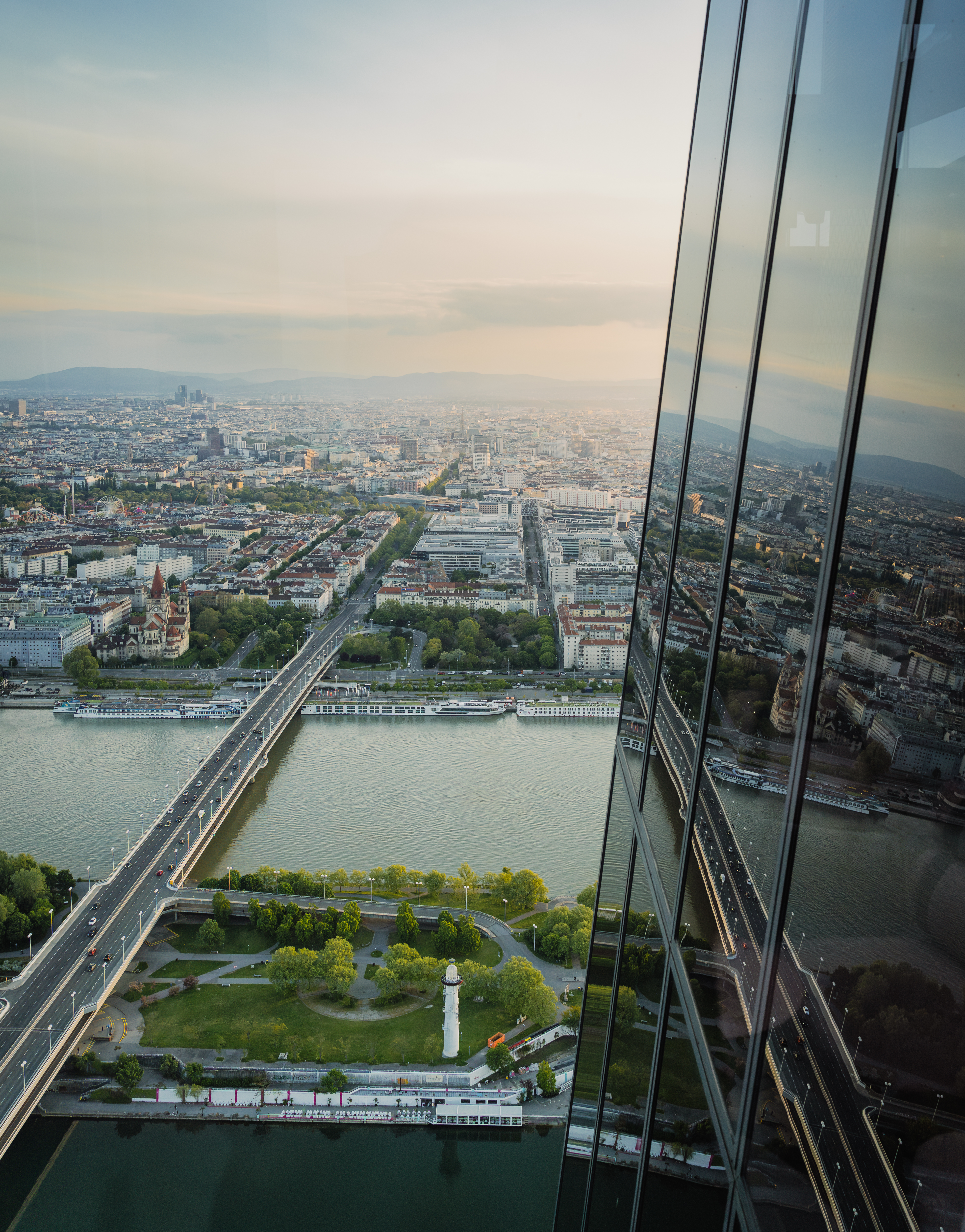Vienna city aerial: Danube River, bridge, park, and reflective skyscraper facade.