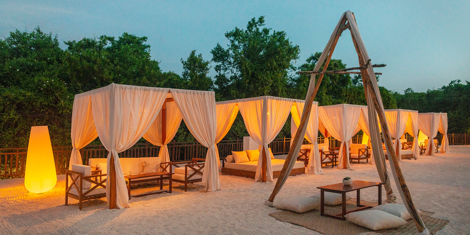 a group of tents with white curtains and wooden tables