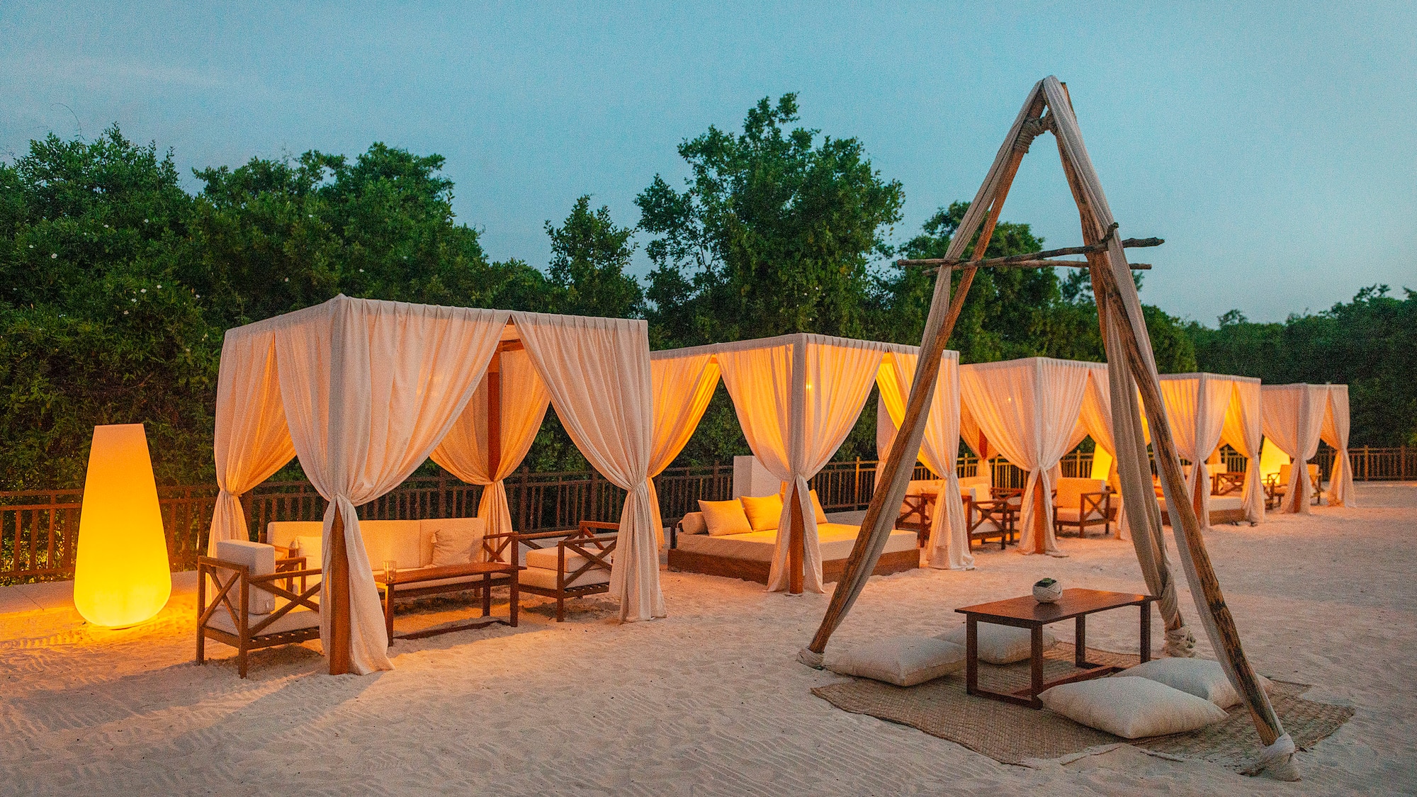 a group of tents with white curtains and wooden tables