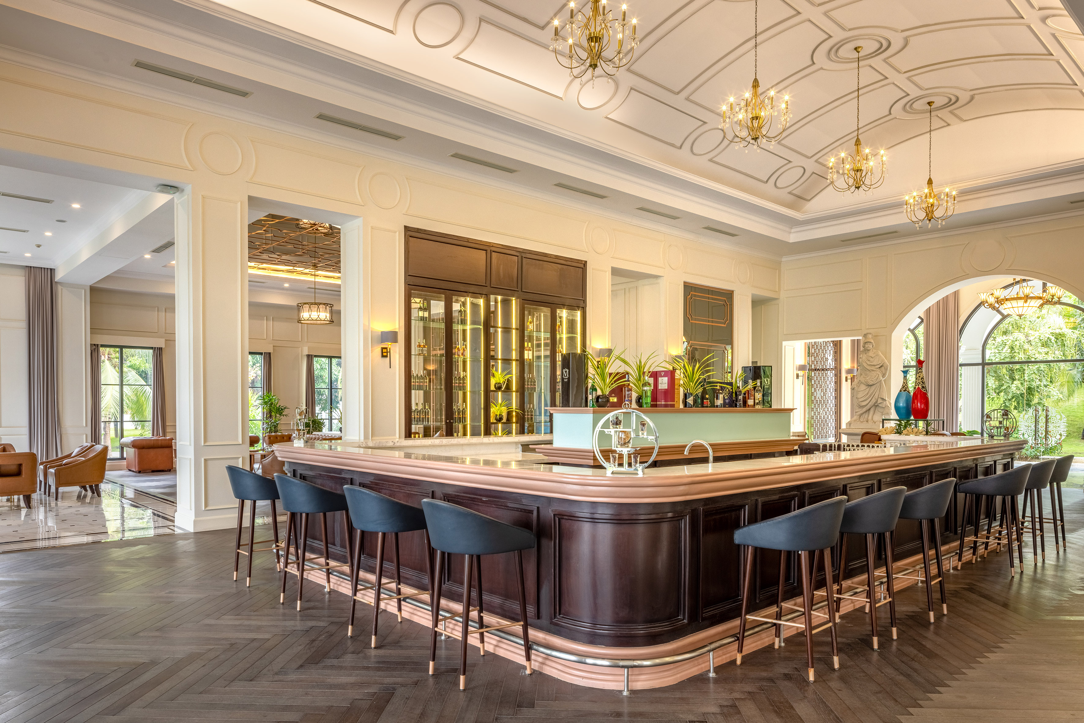 Luxury hotel bar interior with dark wood counter, chic stools, and chandeliers.
