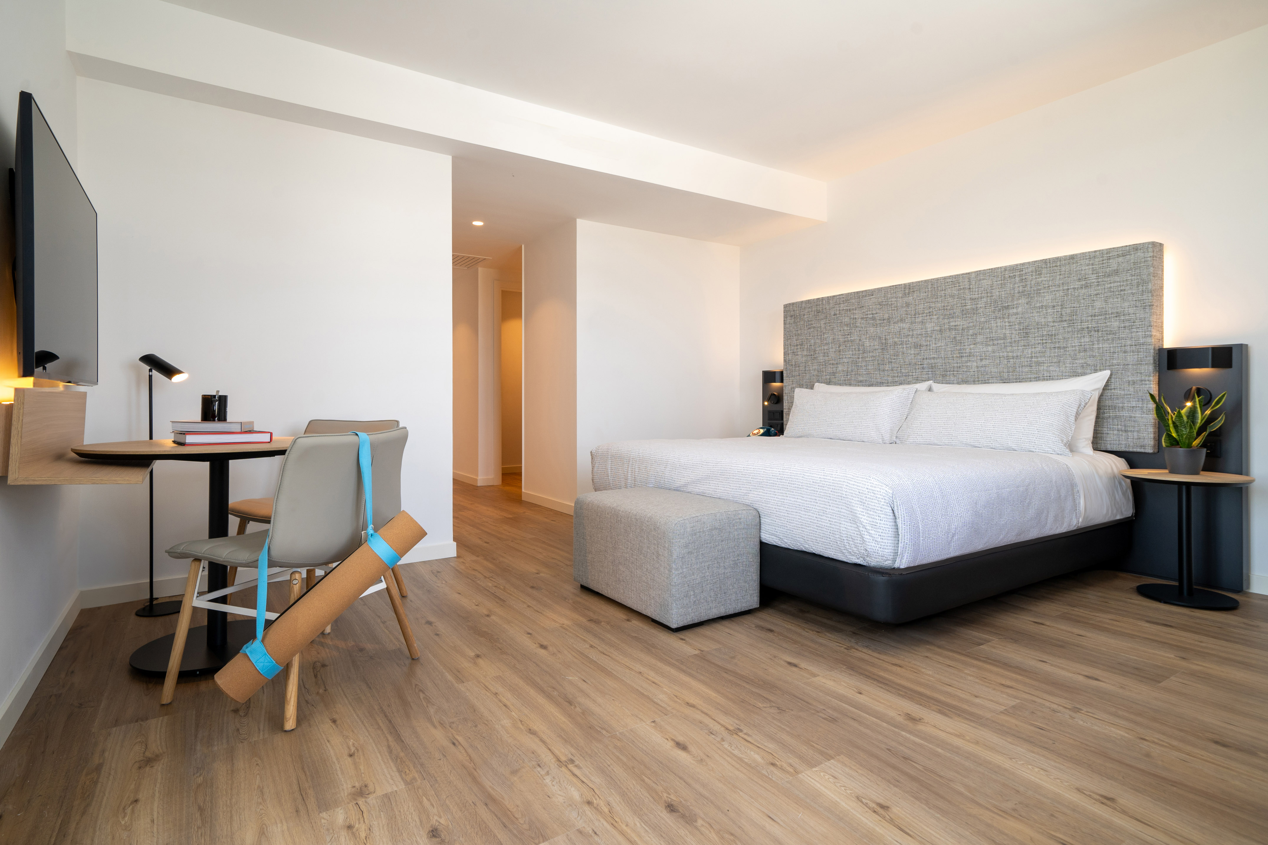 Contemporary hotel room with king bed, desk, yoga mat, and hardwood floors.