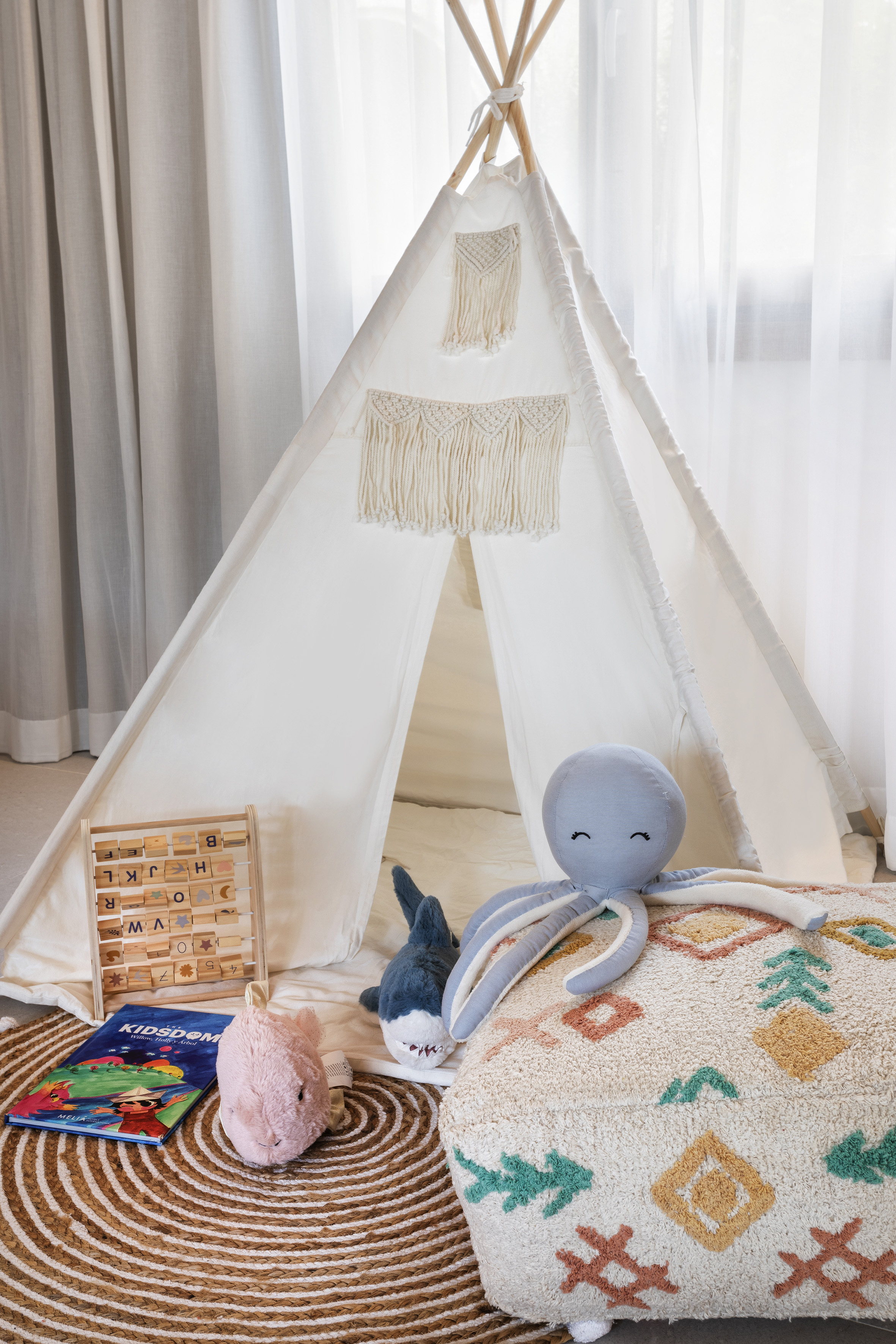 Kids play area with white teepee tent, abacus, plush toys, and colorful pouf.