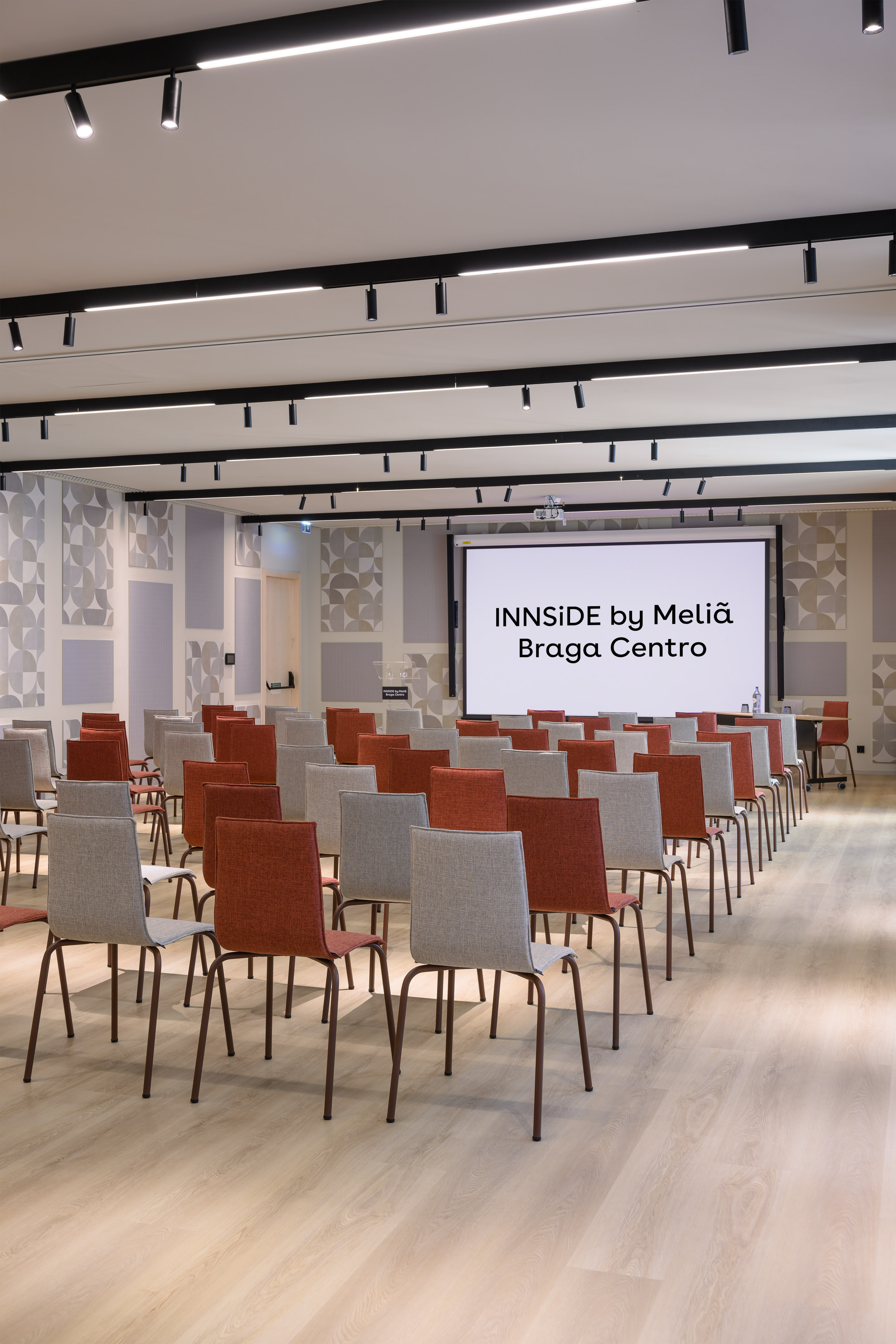 Modern meeting room at INNSiDE Braga Centro with screen and rows of chairs.