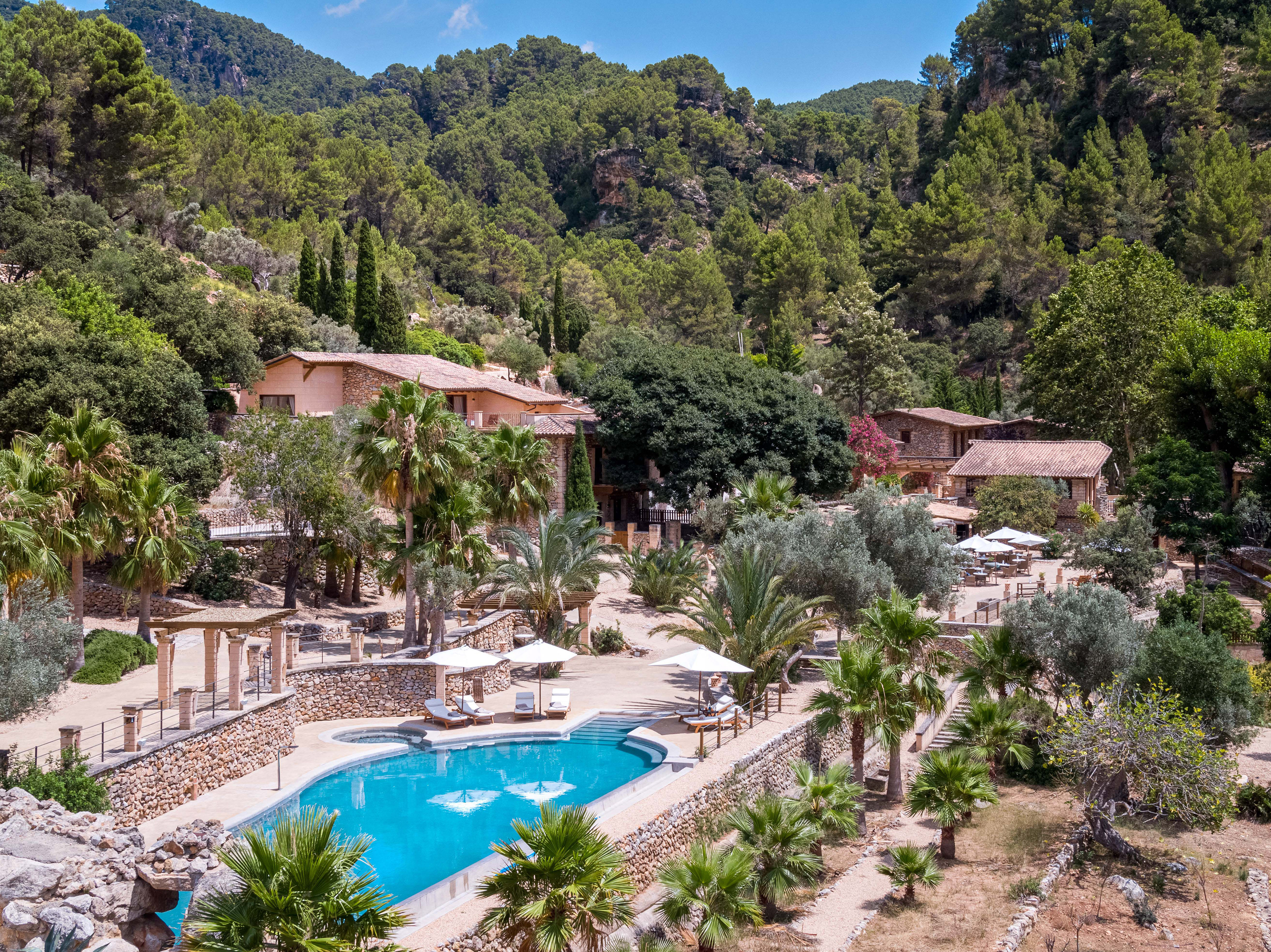 Luxury mountain resort with bright blue pool, palm trees, and stone buildings.