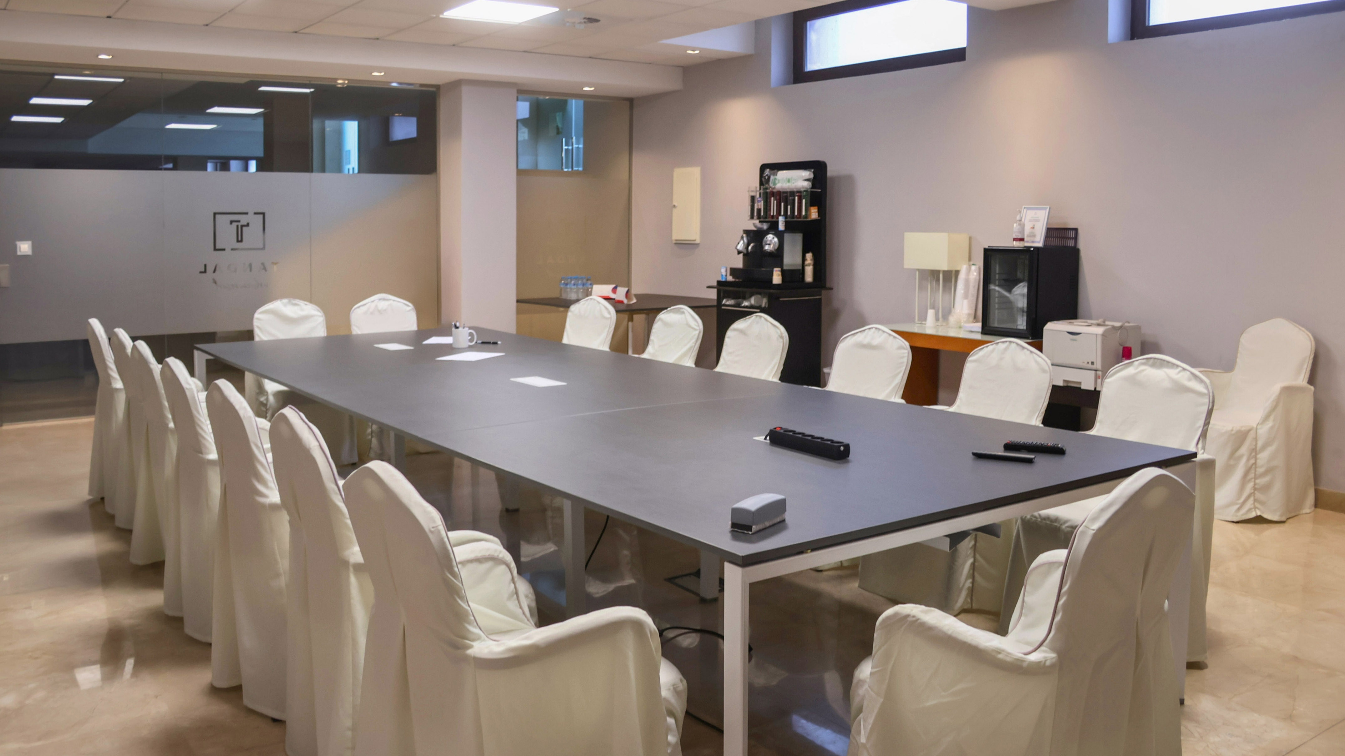 Modern conference room with long dark table, white chairs, and beverage station.