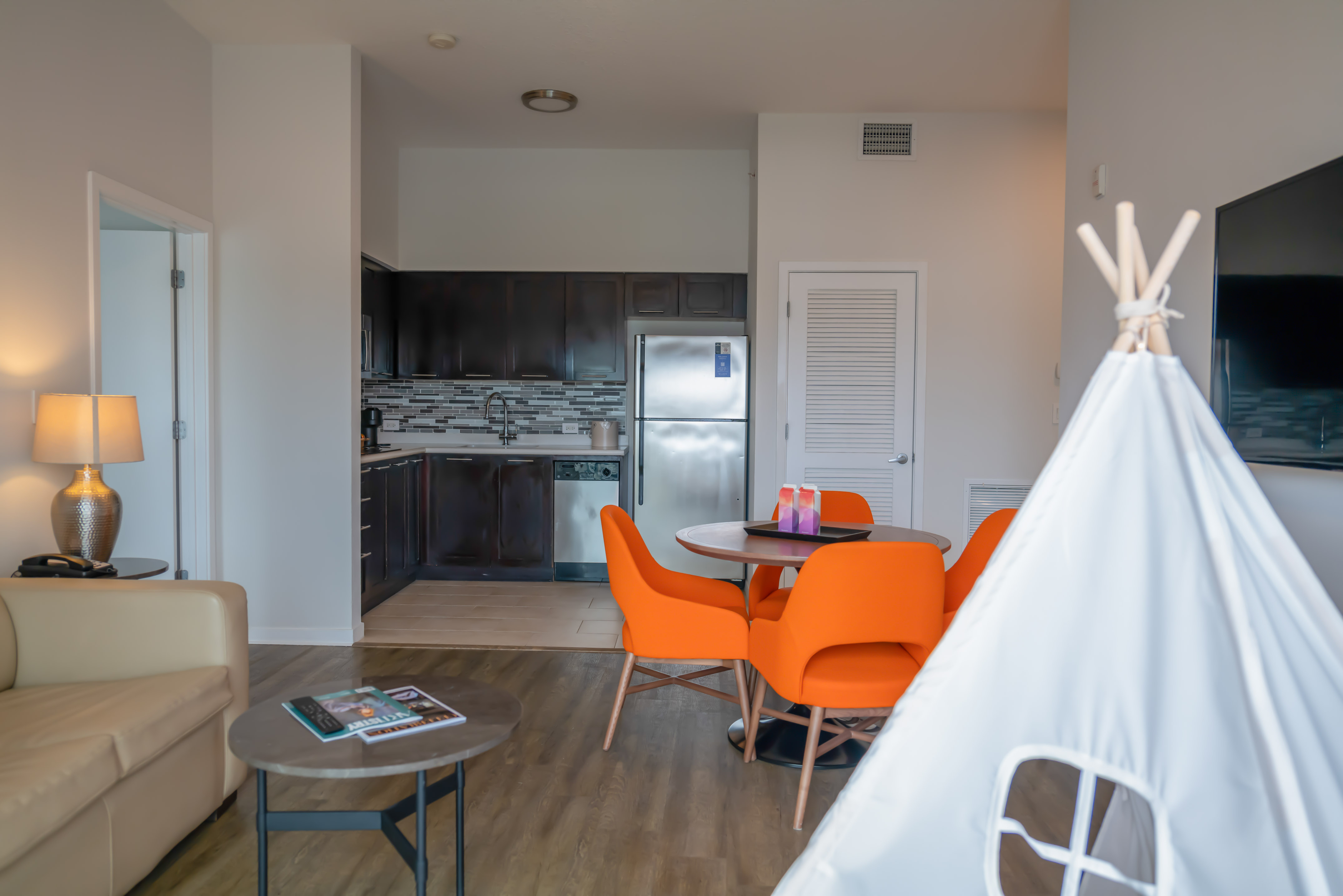 Furnished modern apartment with kitchen, orange dining chairs, and white play teepee. - The Level Family Suite - Meliá Orlando Celebration, Orlando