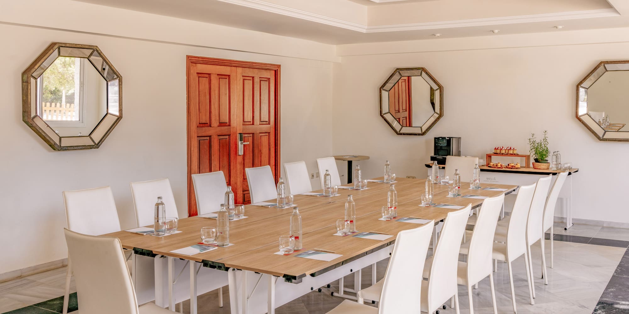 Conference room with long wooden table, white chairs, and refreshments.