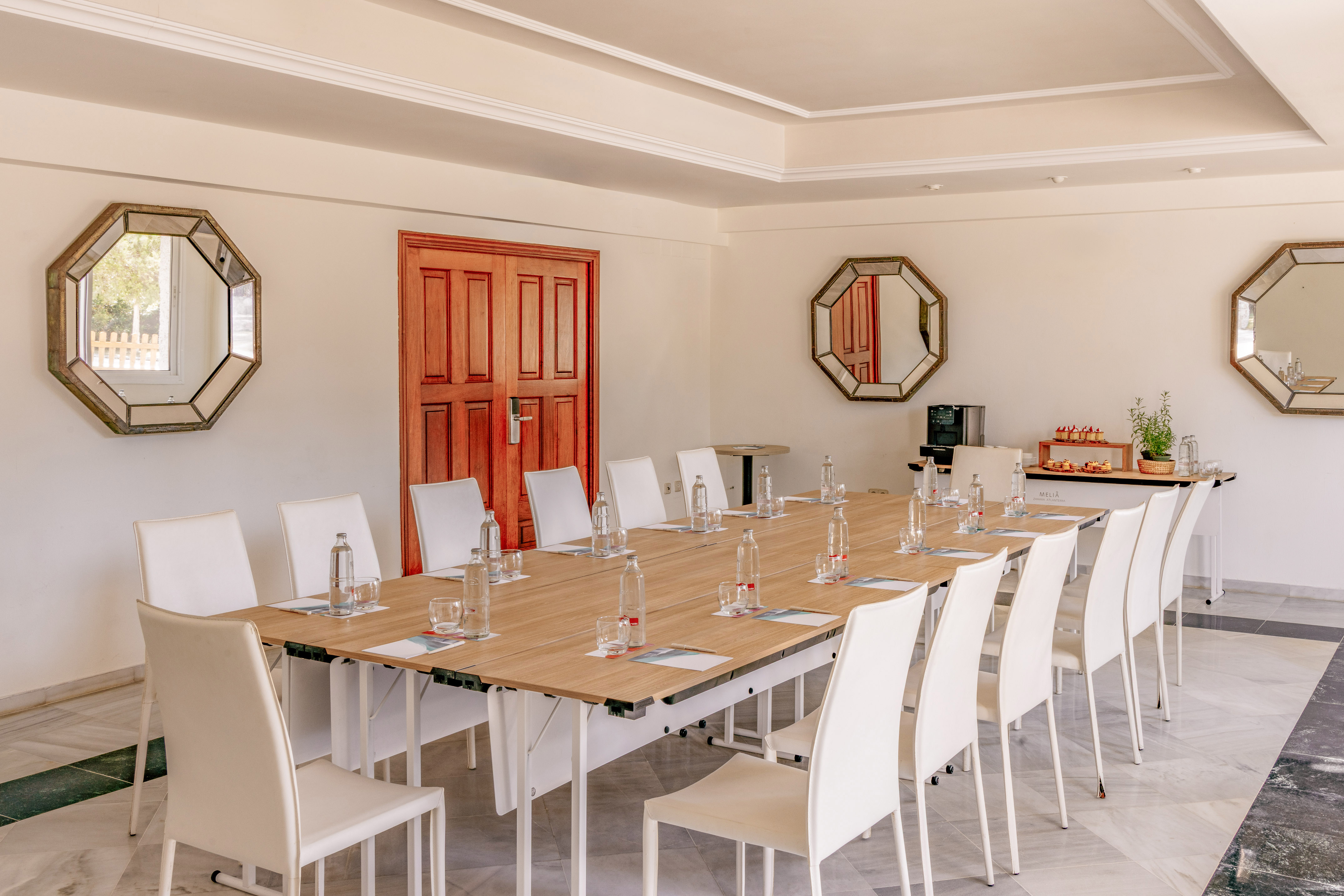 Conference room with long wooden table, white chairs, and refreshments.