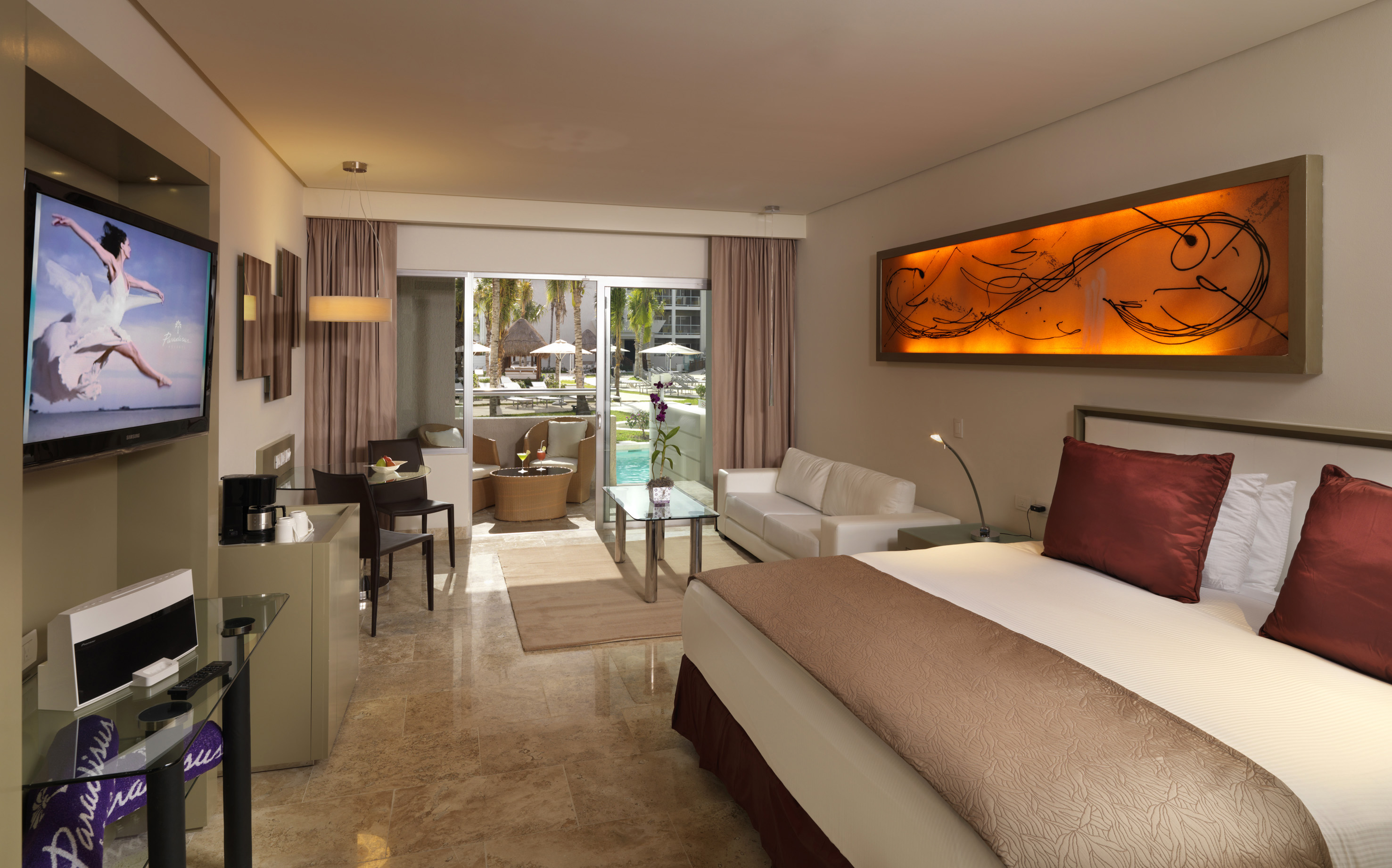 Spacious hotel suite featuring a bed, sofa, TV, and balcony with pool view.
