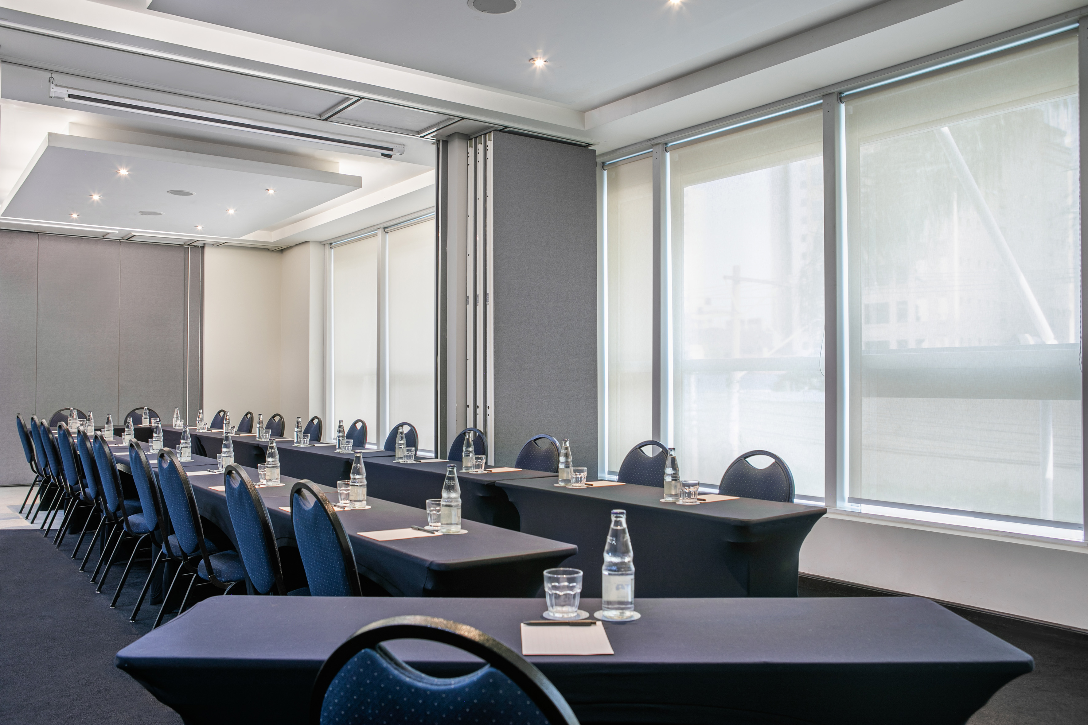 Modern conference room with blue chairs, dark tables, water bottles, and bright windows.