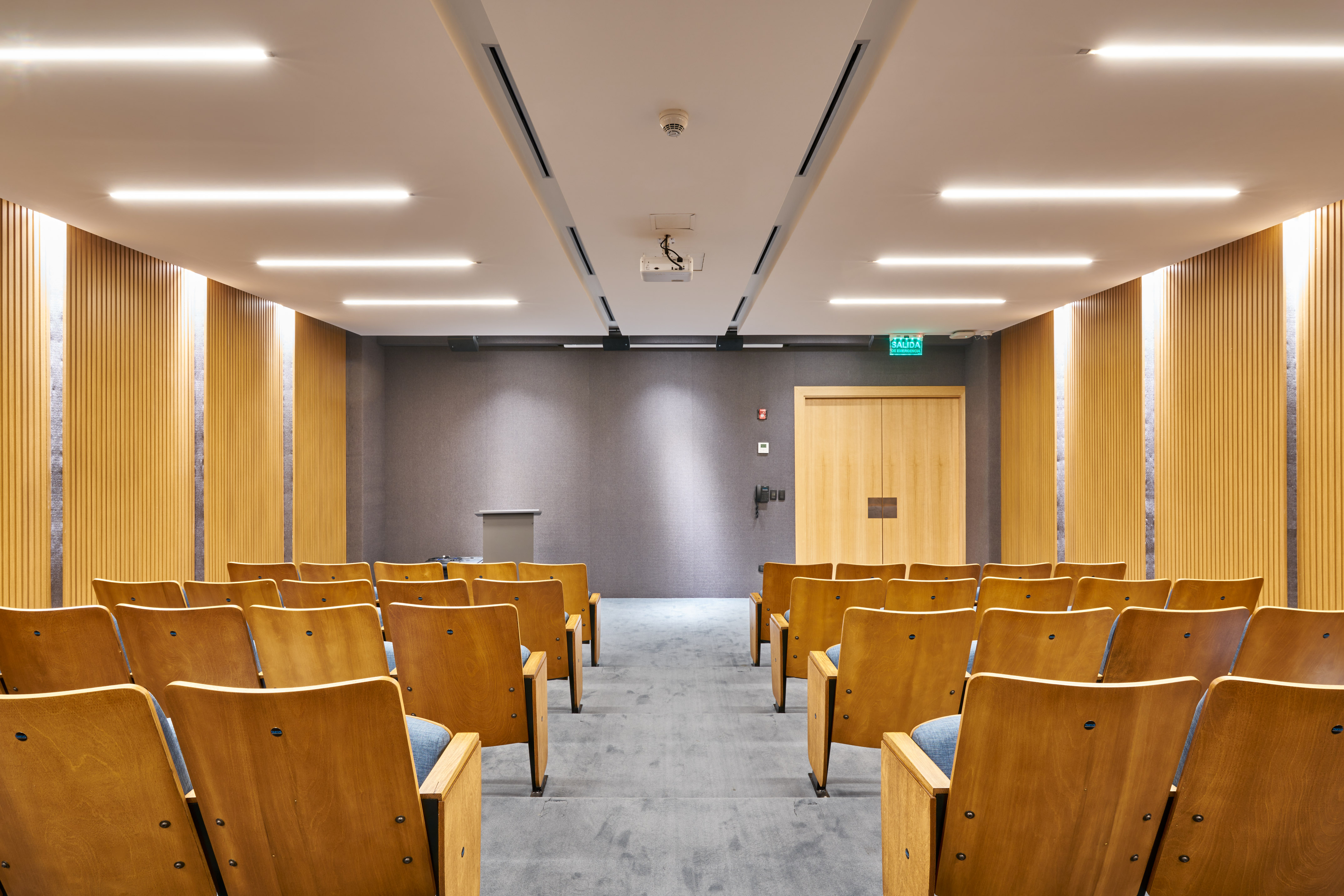 Empty lecture hall with wooden chairs, projector, and modern design.