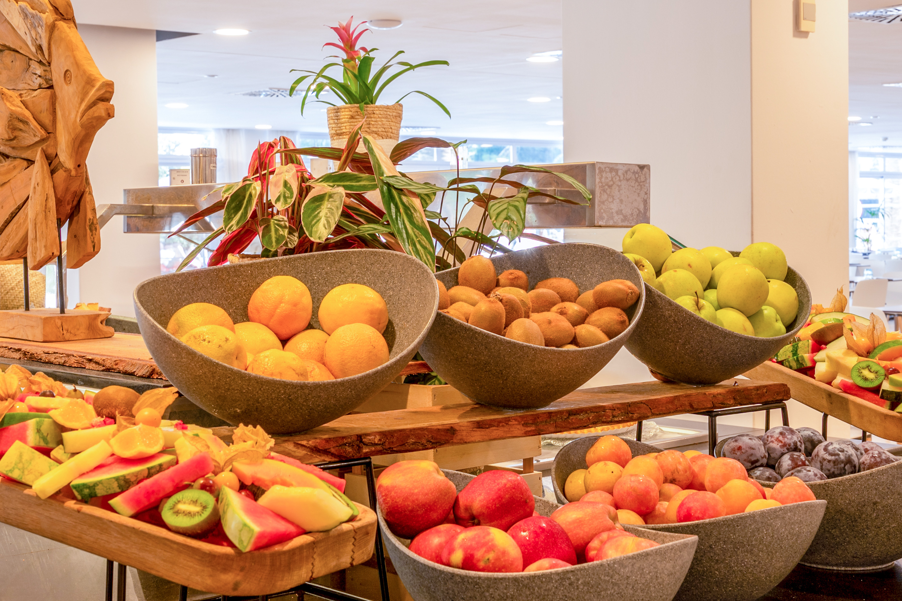 Fresh fruit buffet display: oranges, kiwis, apples, watermelon, plums.