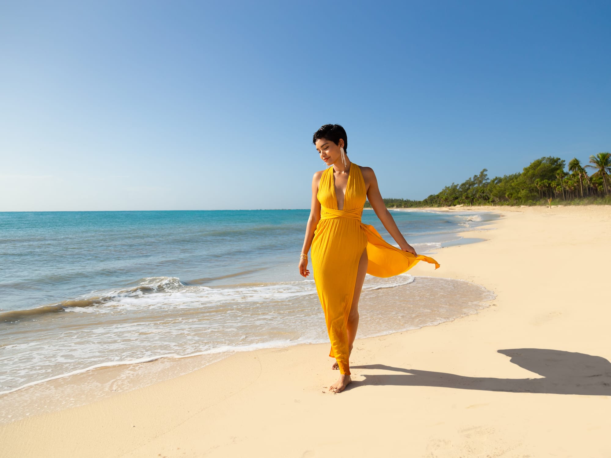 a woman in a yellow dress walking on a beach