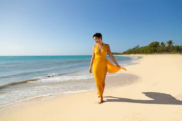 a woman in a yellow dress walking on a beach