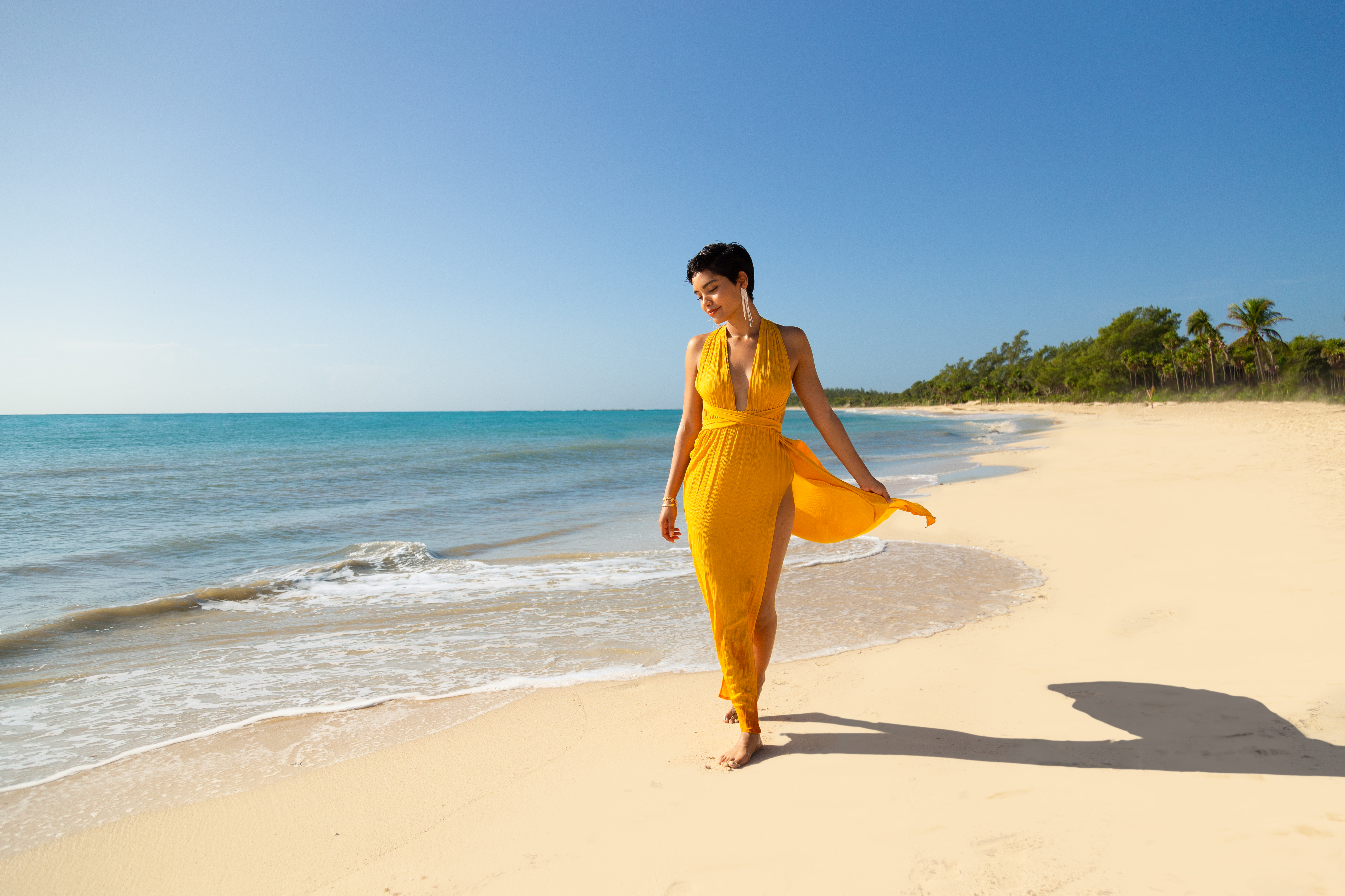 a woman in a yellow dress walking on a beach