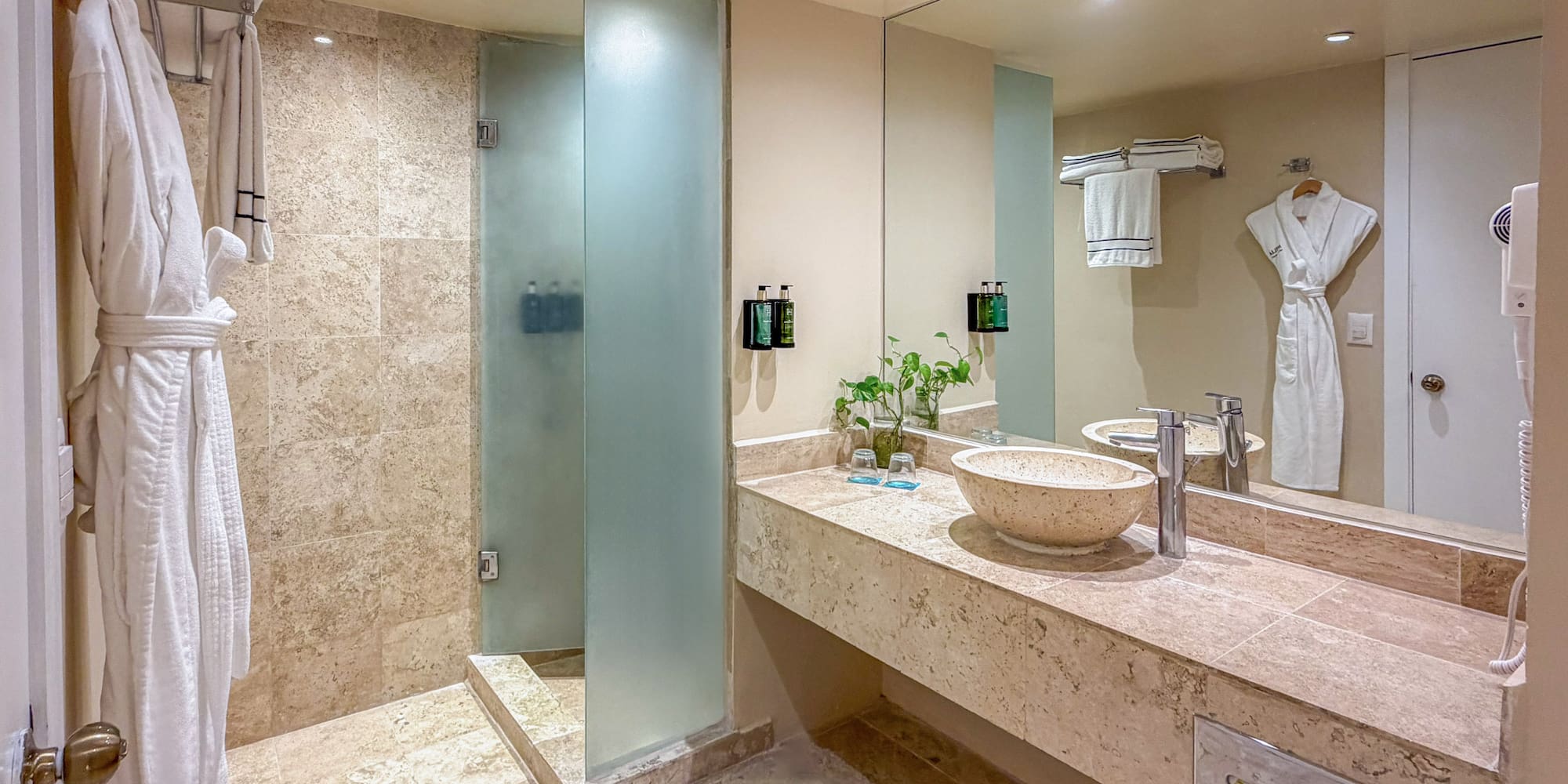 Modern hotel bathroom with walk-in shower, stone vanity, vessel sink, and white robes.