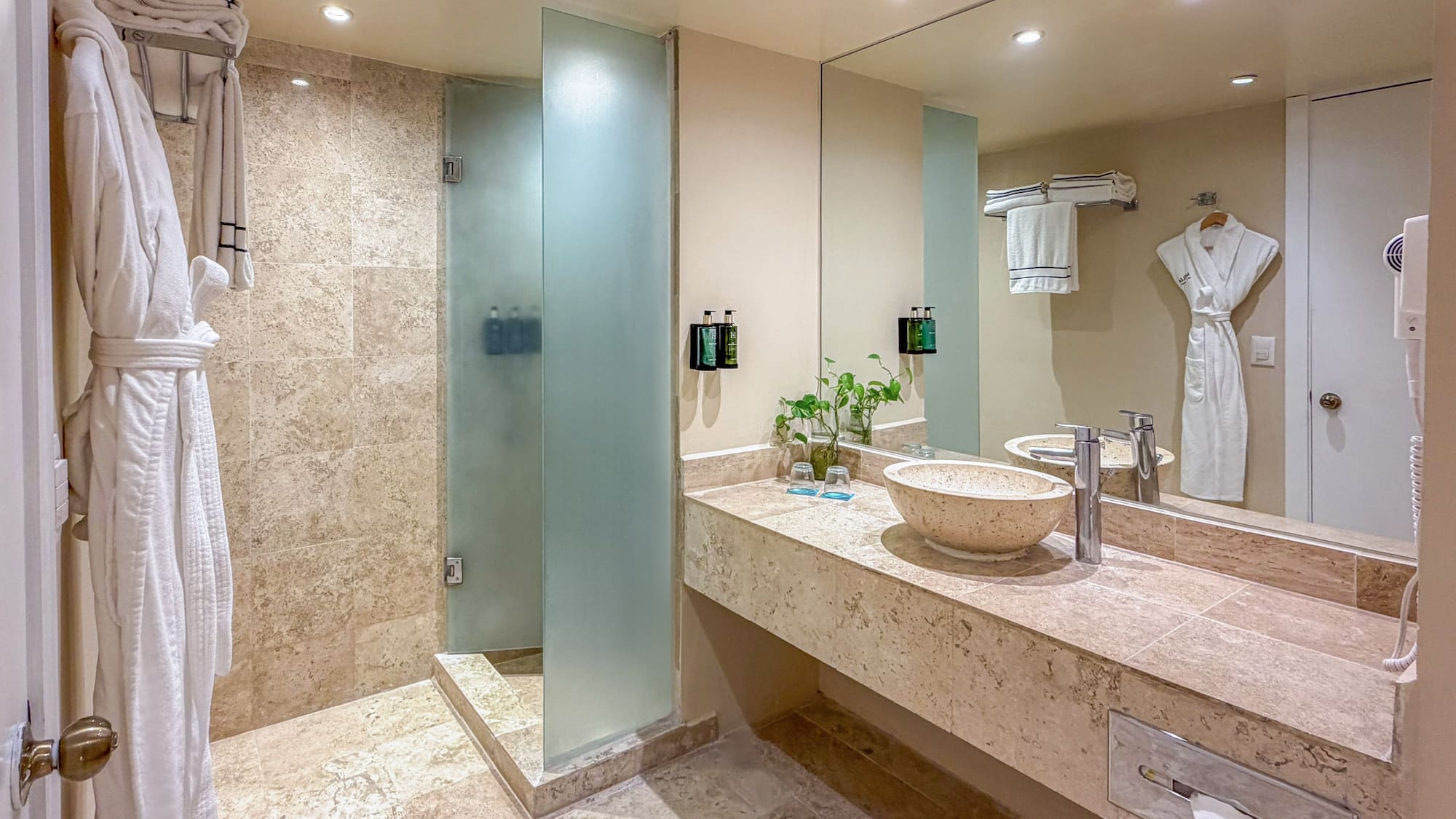 Modern hotel bathroom with tiled shower, stone vanity, and vessel sink.
