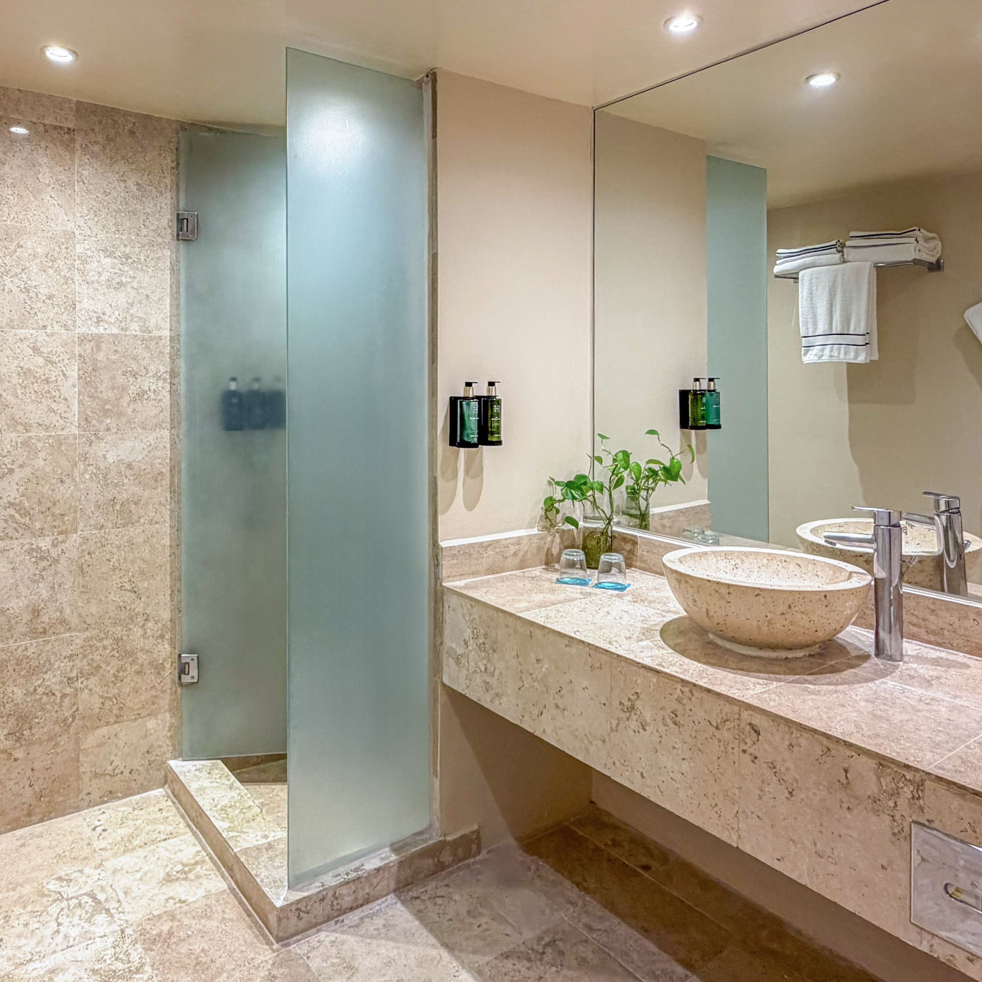 Modern hotel bathroom with tiled shower, stone vanity, and vessel sink.