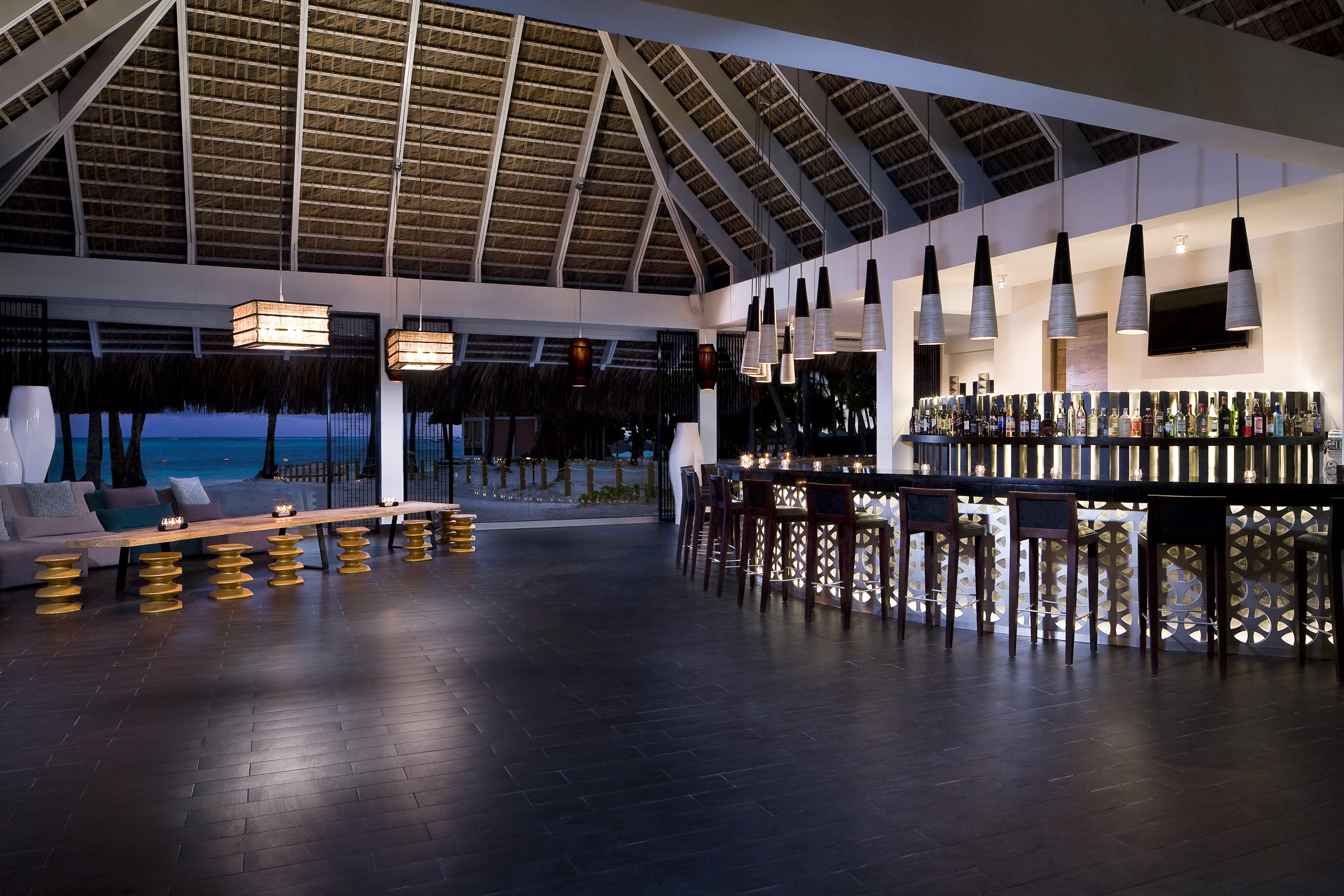 Tropical resort bar with thatched roof, lounge, and evening ocean view.