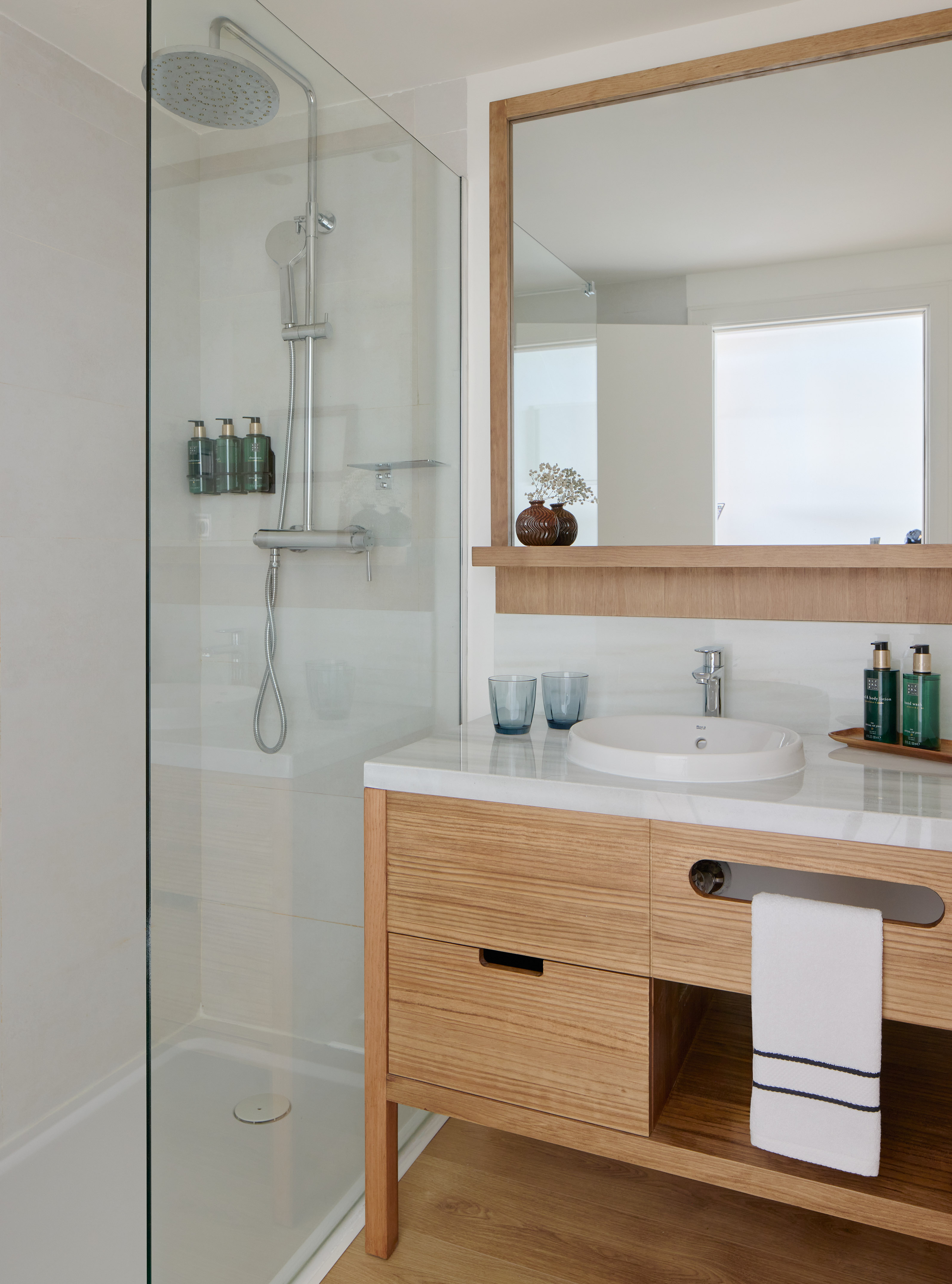 Modern bathroom with glass shower, wood vanity, white sink, and mirror.