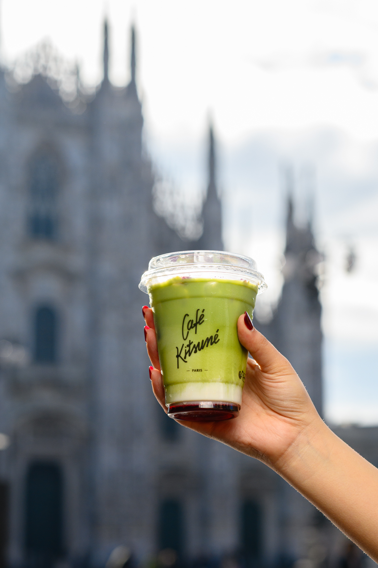 Café Kitsuné iced matcha latte held in hand, blurred Milan Duomo.