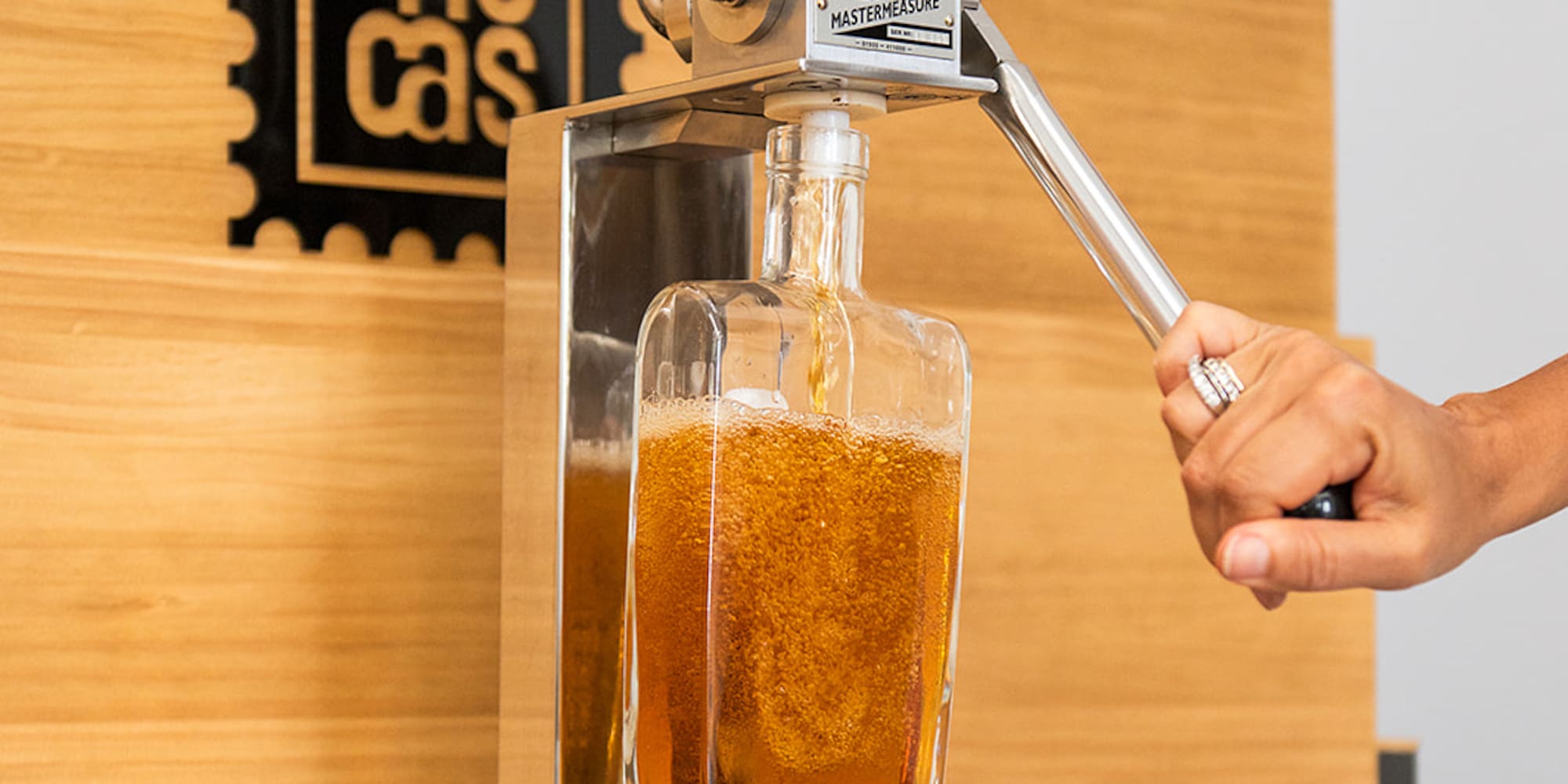 a hand holding a metal tool to a glass bottle with a liquid in it