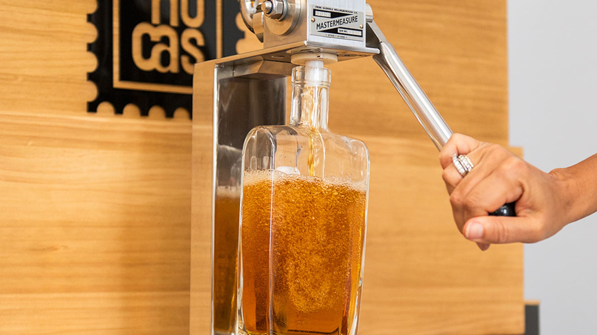 a hand holding a metal tool to a glass bottle with a liquid in it