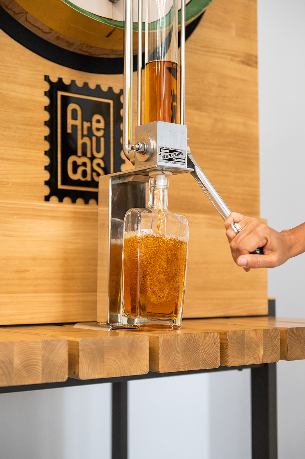 a hand holding a metal tool to a glass bottle with a liquid in it