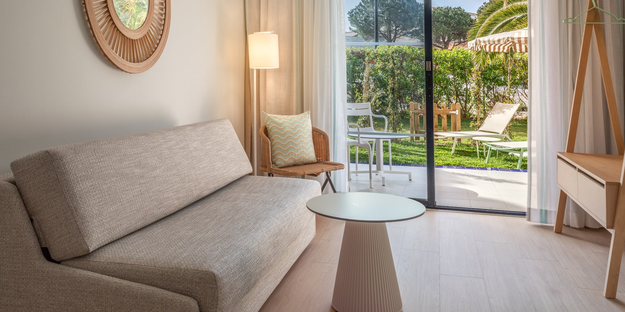 Bright hotel living room with sofa, patio garden view, and modern decor.