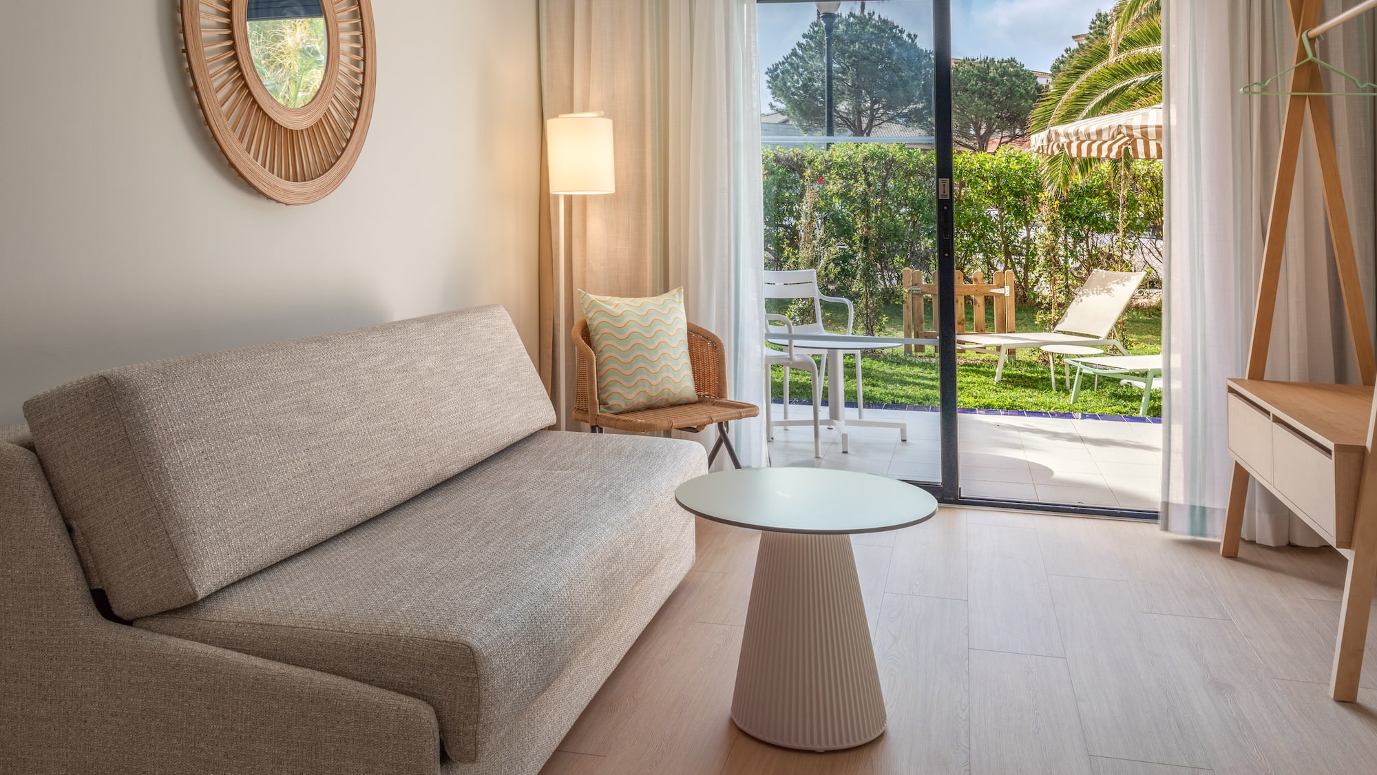 Modern hotel room with sofa, coffee table, and glass doors to garden patio.
