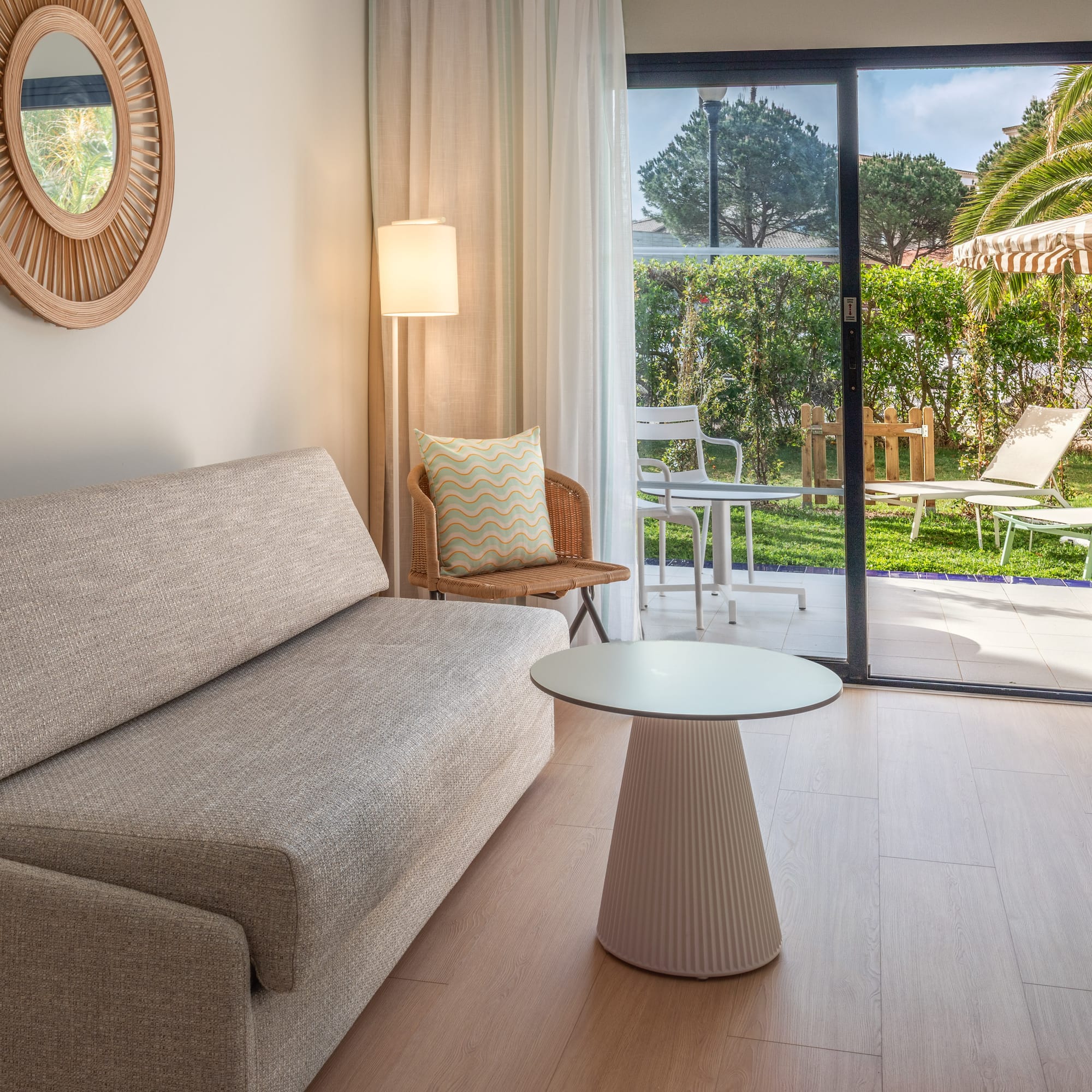 Bright hotel living room with sofa, patio garden view, and modern decor.