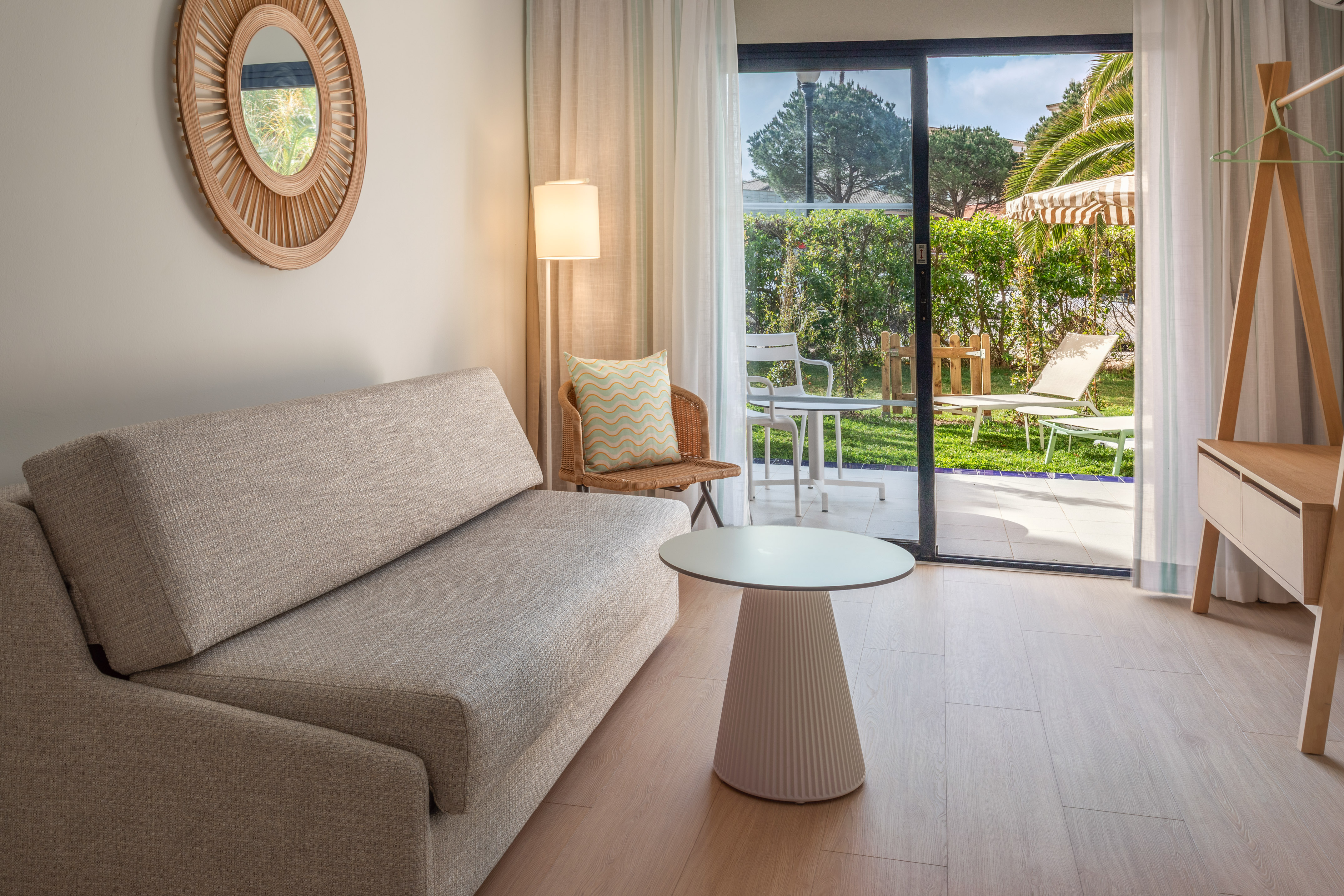 Modern hotel room with sofa, coffee table, and glass doors to garden patio.