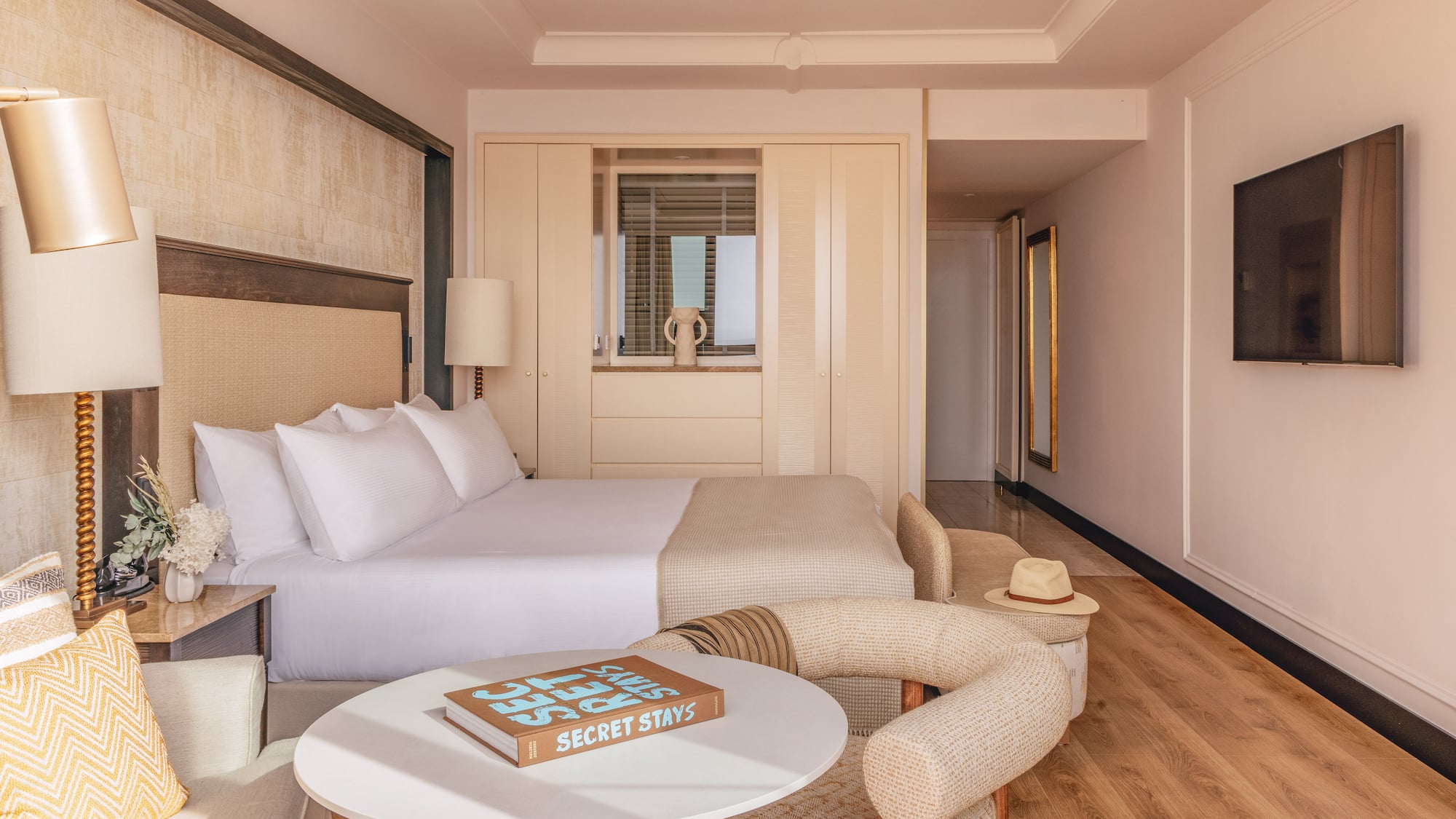 Modern hotel suite: large bed, neutral decor, wood floors, and elegant furnishings.