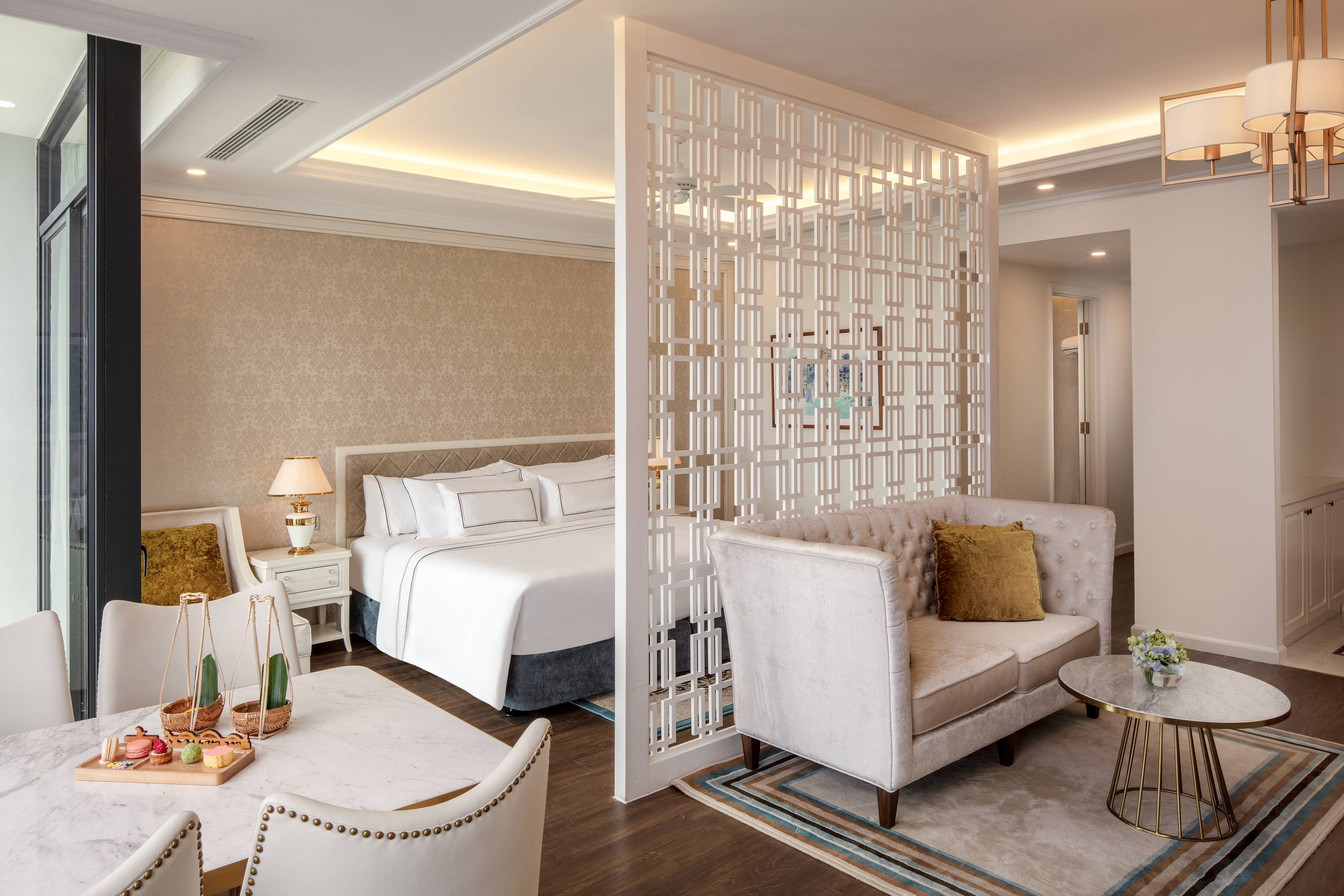 Elegant hotel suite with bed, sofa, dining table, and decorative divider.