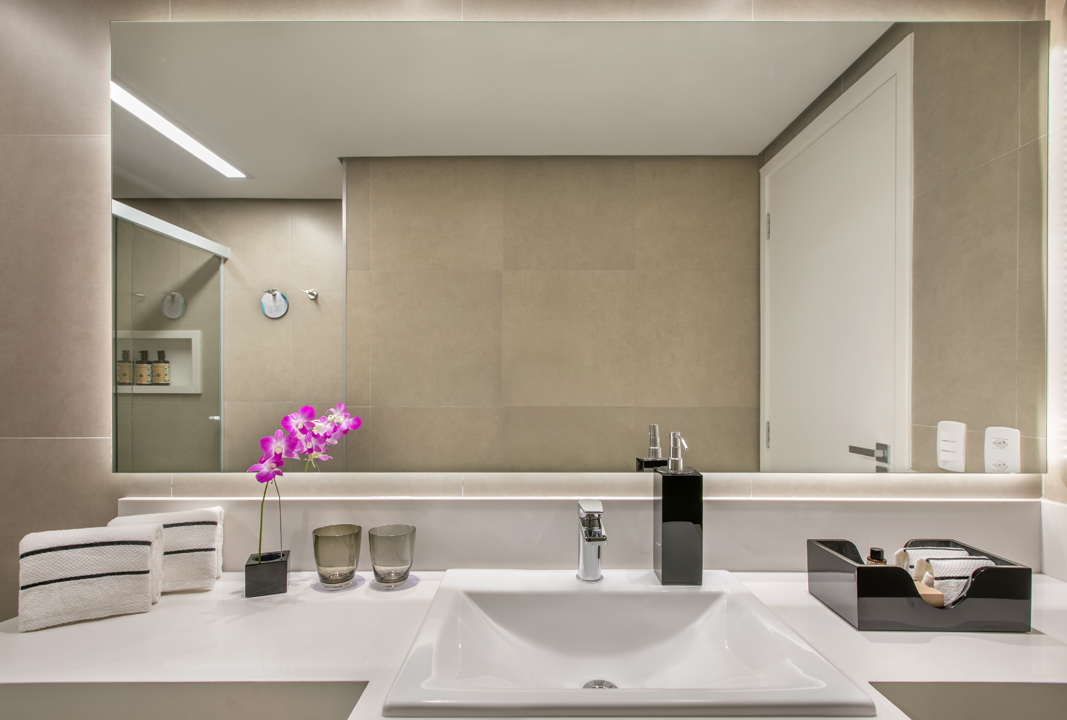 Modern bathroom vanity with white sink, large mirror, purple orchid, and towels.