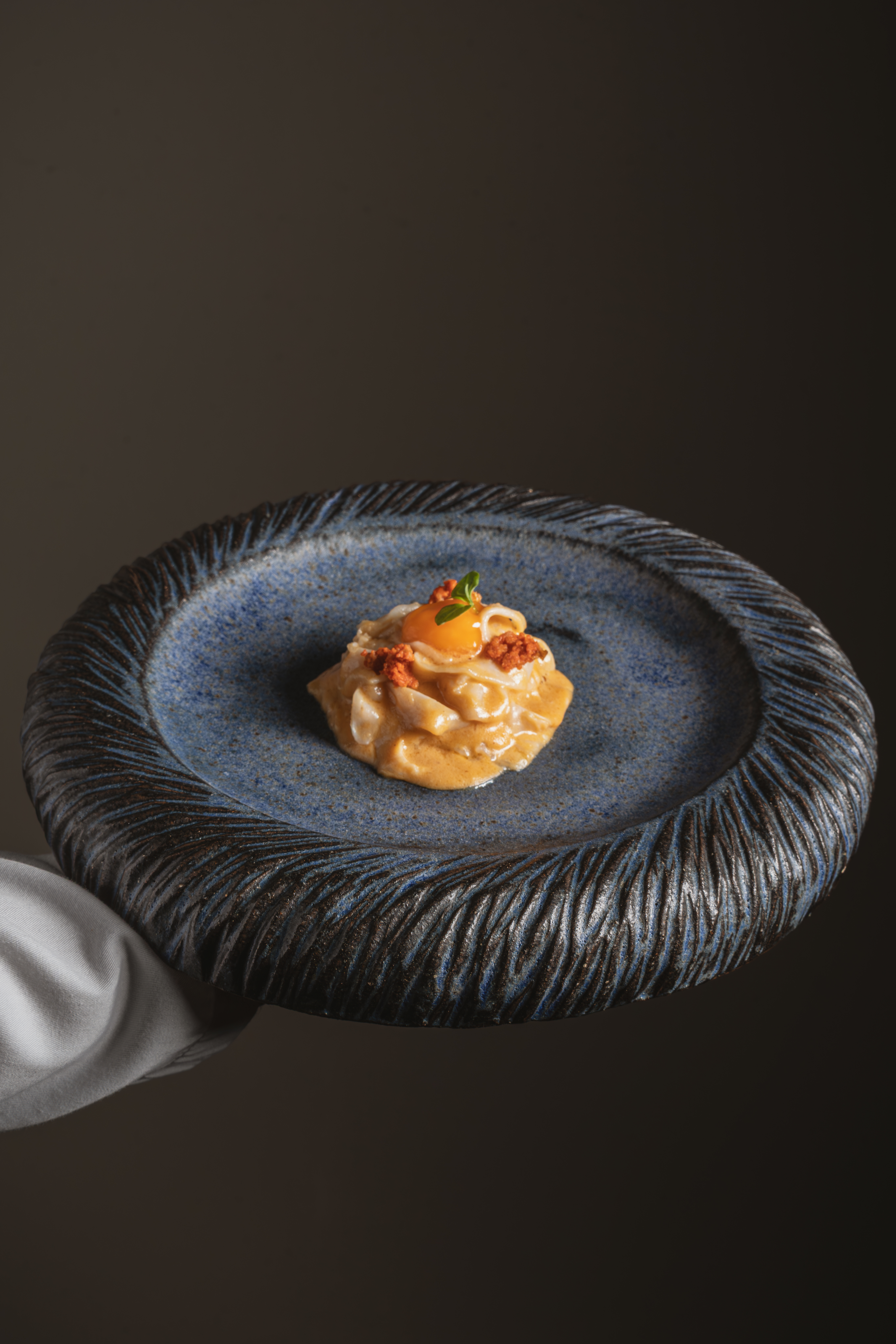 Fine dining pasta with egg yolk on a textured blue plate.