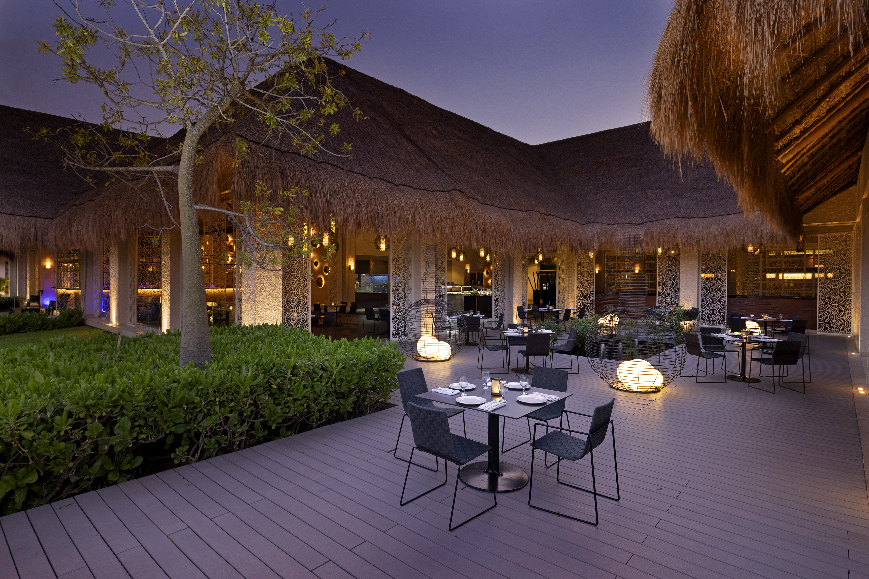 Evening dining terrace with thatched roof restaurant and ambient lighting.