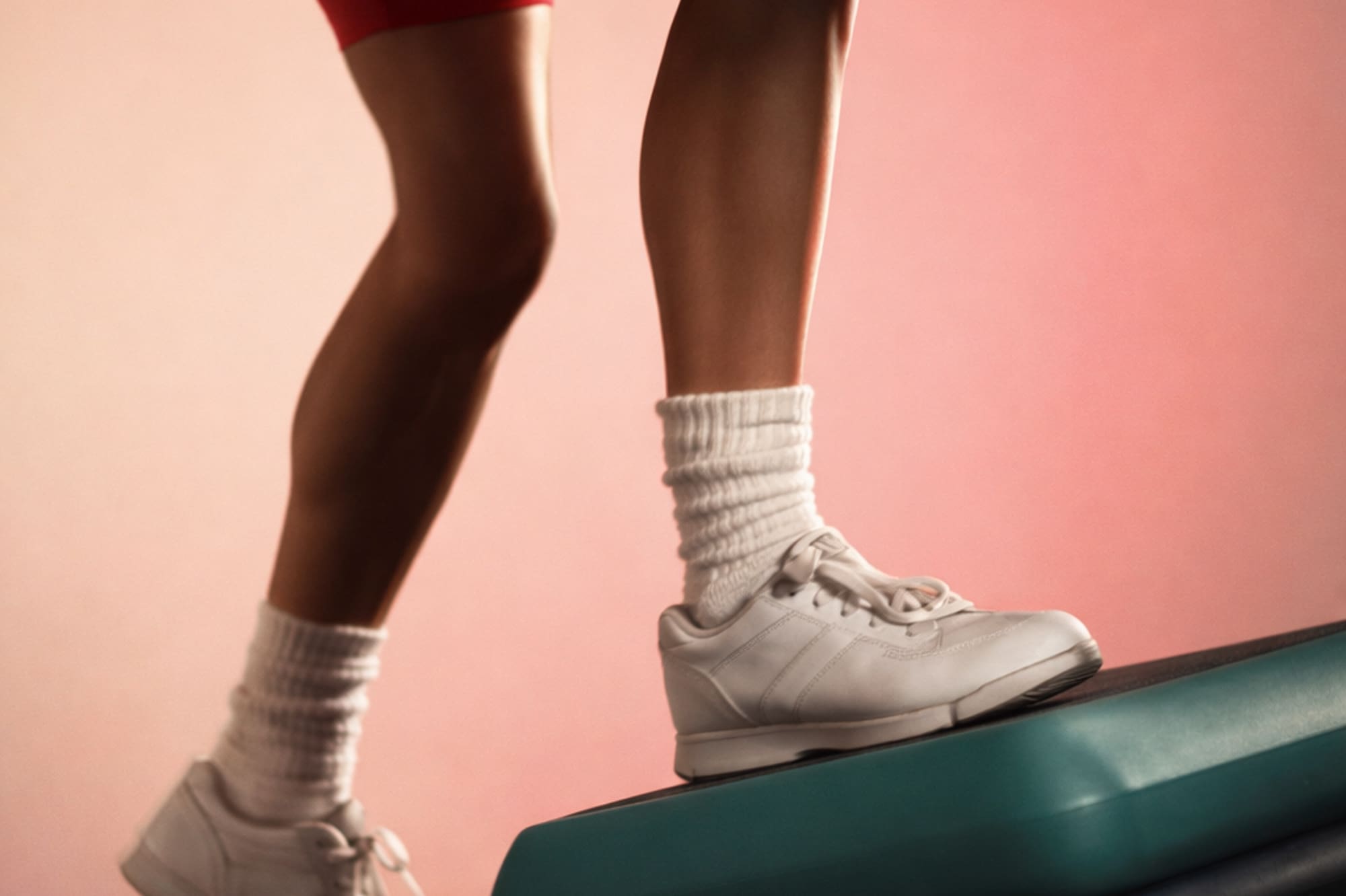 Person in red shorts and white sneakers stepping onto aerobics platforms.
