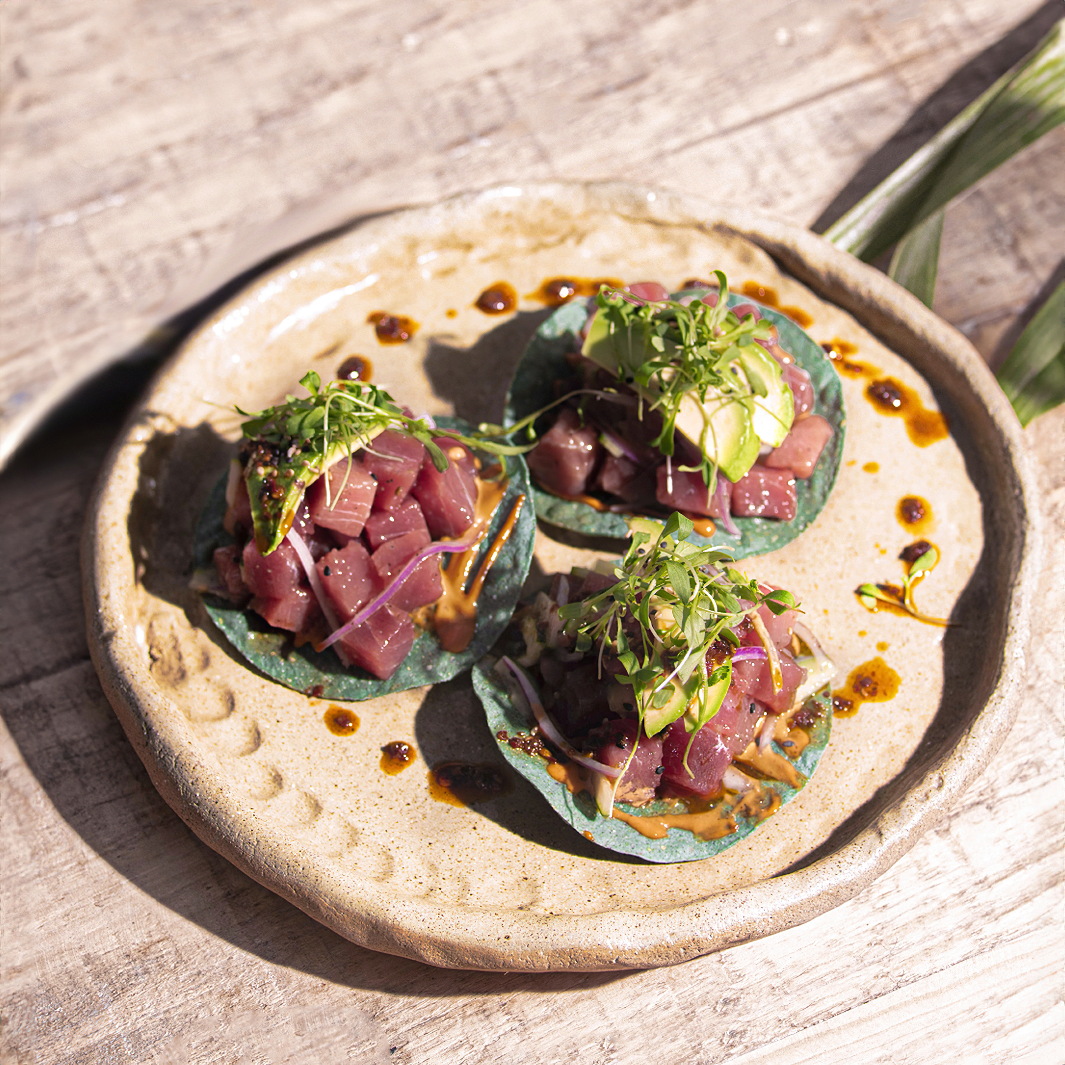 Ahi tuna tacos with avocado, red onion, microgreens on blue tortillas.