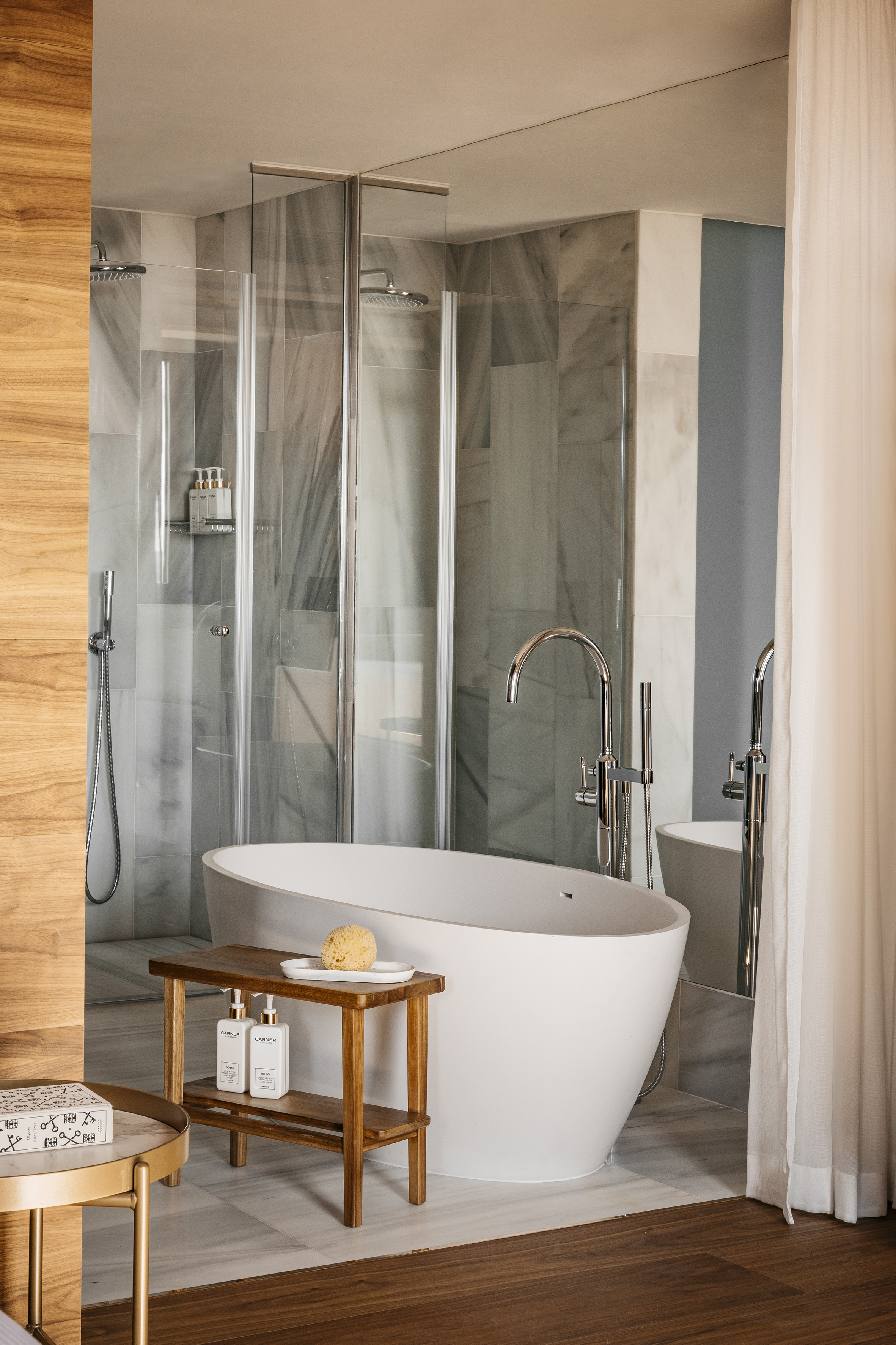 Modern luxury bathroom with freestanding tub, glass shower, marble walls, and wood accents.