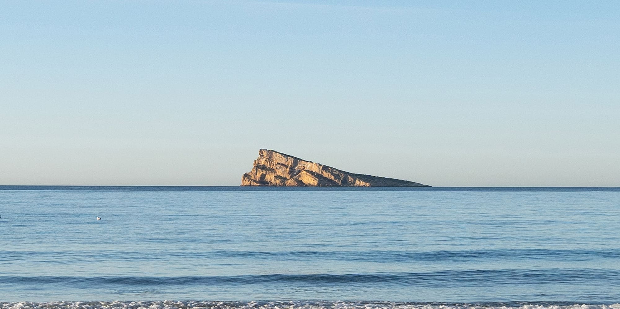 a sandy beach with a rock in the water