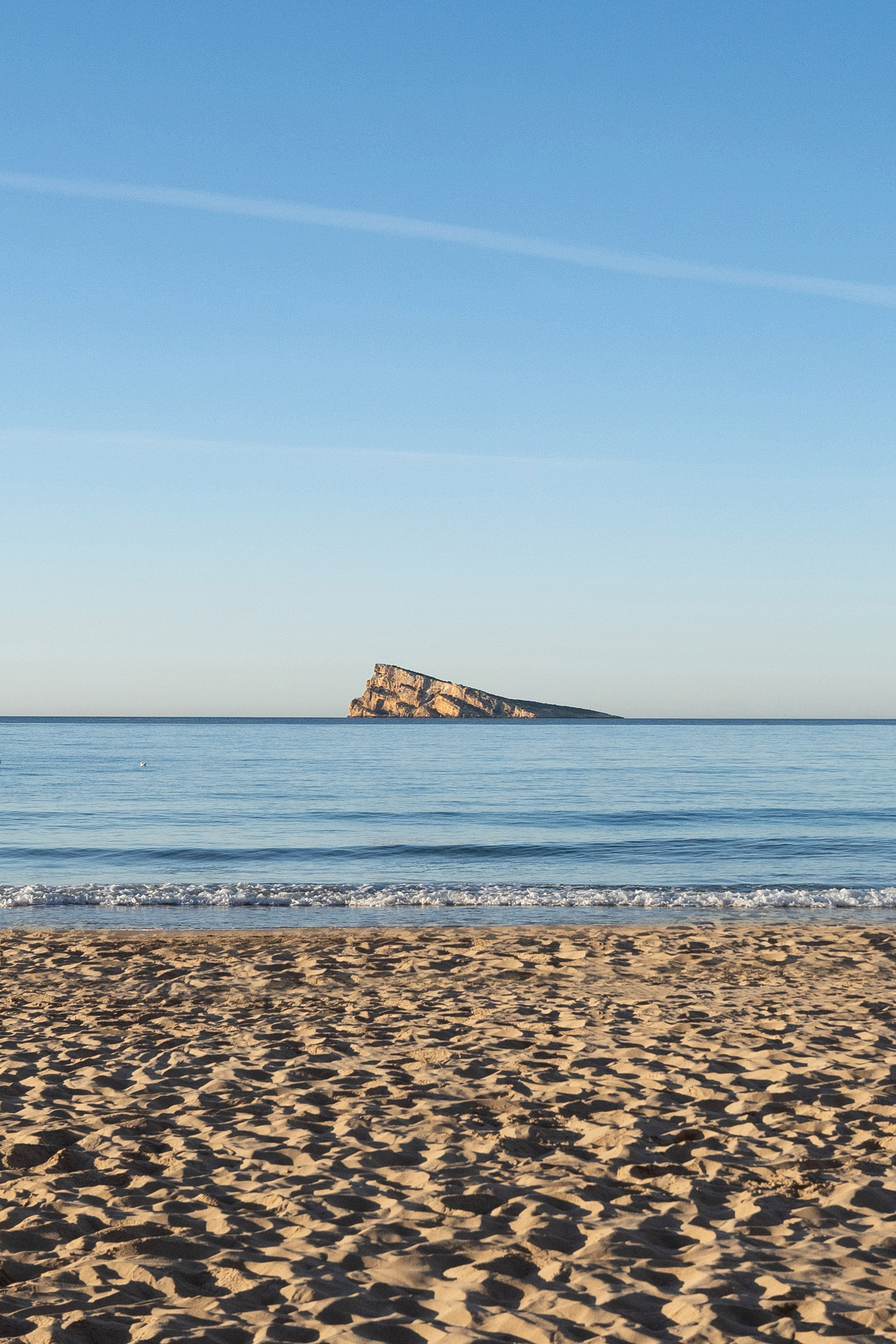 Benidorm beach, blue sea with gentle waves, and distant rocky island.